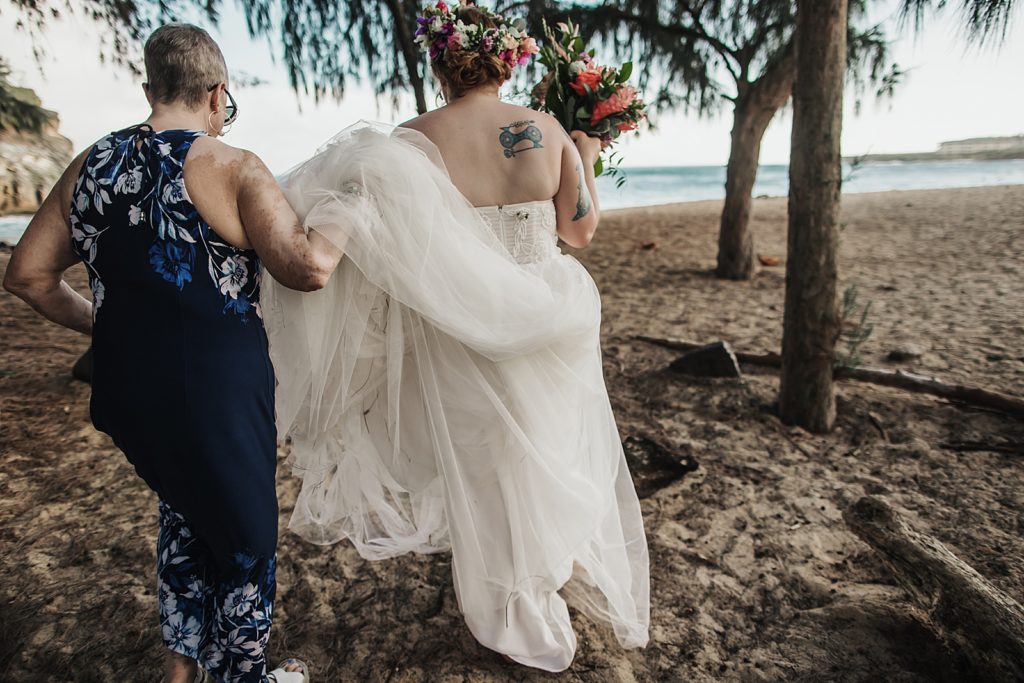Mother helping Bride by holding wedding train on sand on the beach 