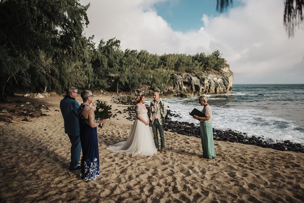 Bride and Groom standing together on the sand with one set of parents and officiant