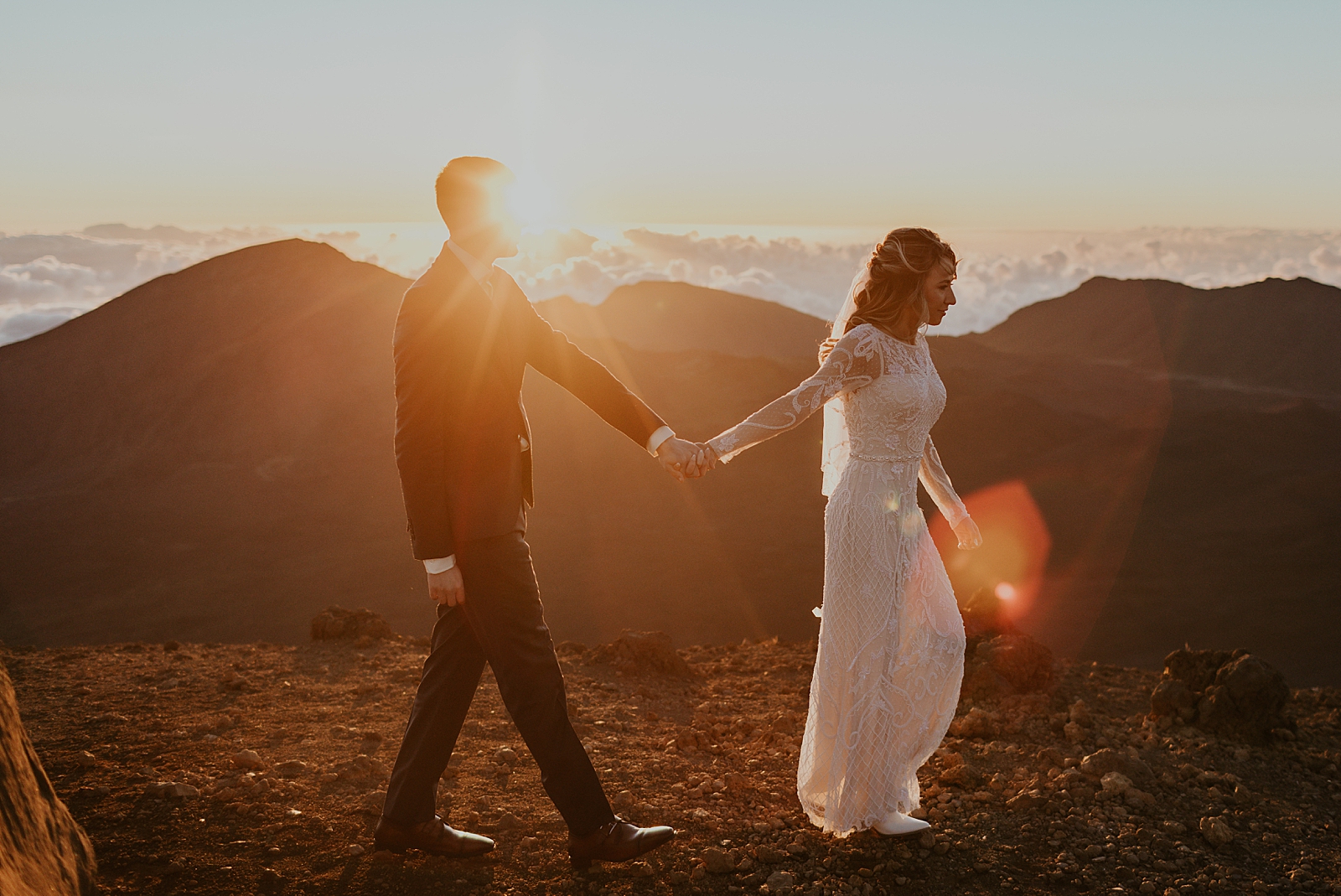 Bride and Groom holding hands and walking on a mountain as the sunsets