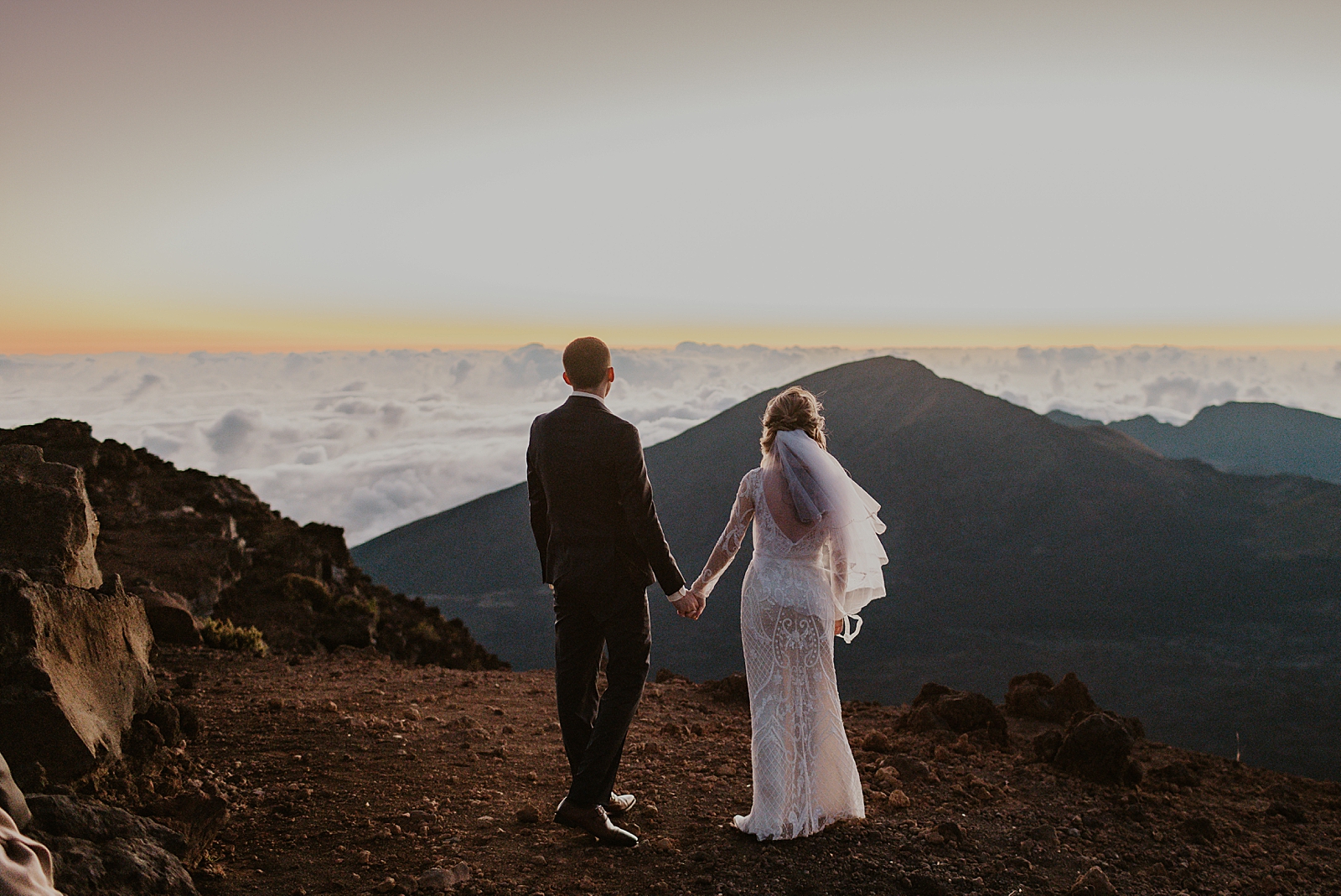 Bride and Groom holding hands and looking at the clouds on top of a mountain