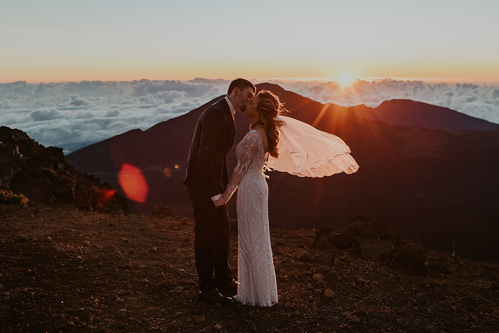 Bride and Groom kissing as the sun sets on the clouds
