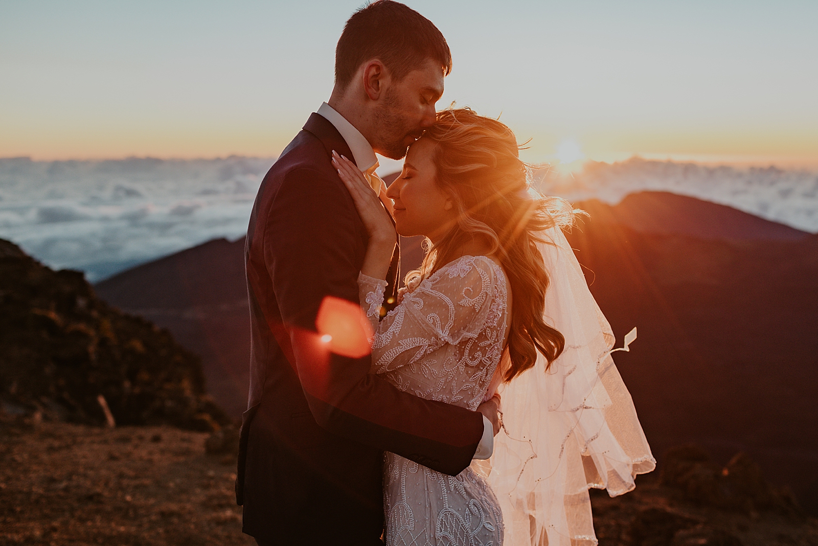 Groom holding Bride and kissing her on the forehead on the mountain