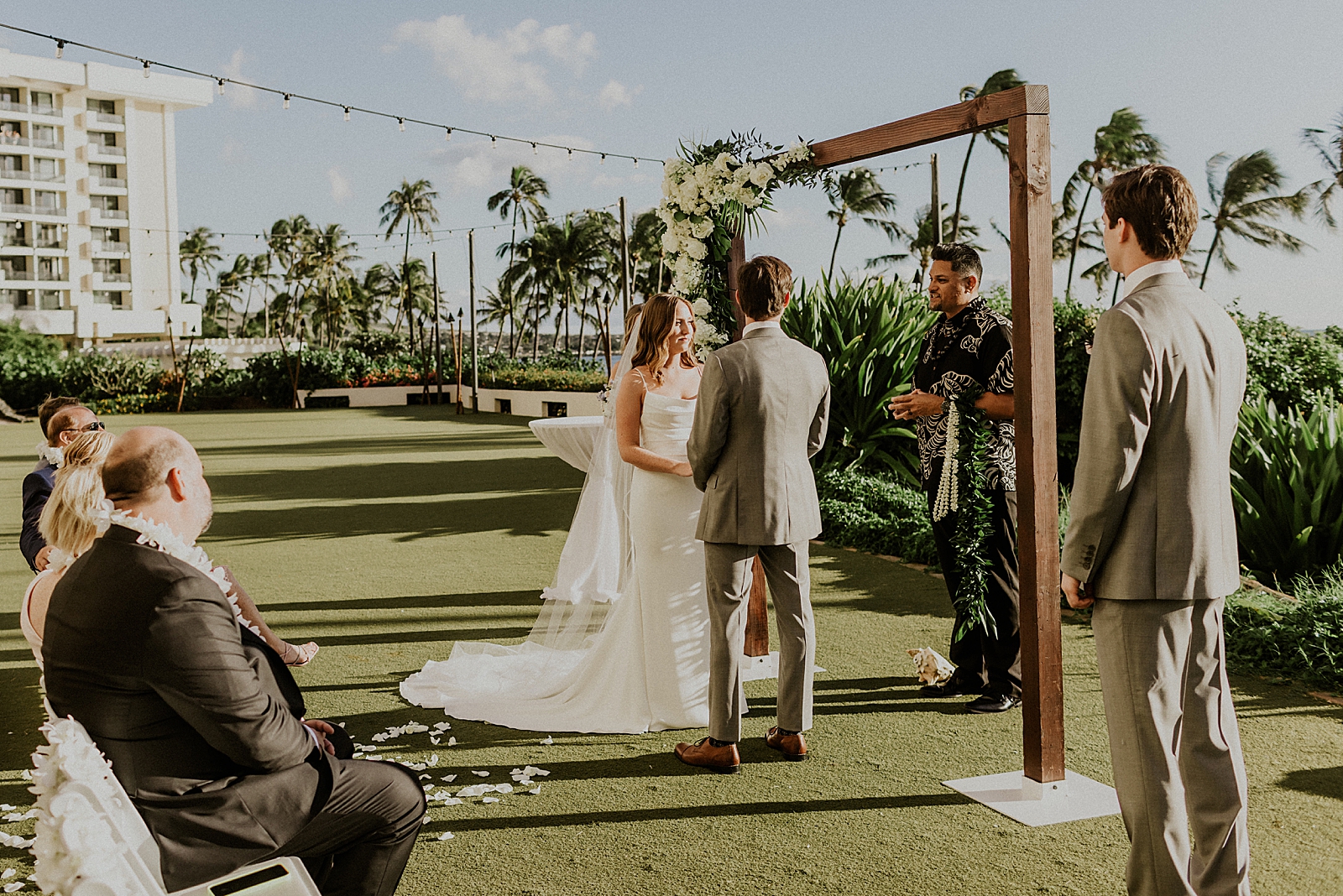 Bride and Groom holding hands and looking at officiant for outdoor Ceremony by greenery and palm trees