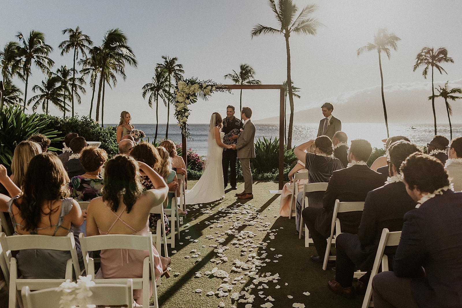 Wide shot of Bride and Groom holding hands with the ocean in front of them and guests watching outdoor Ceremony