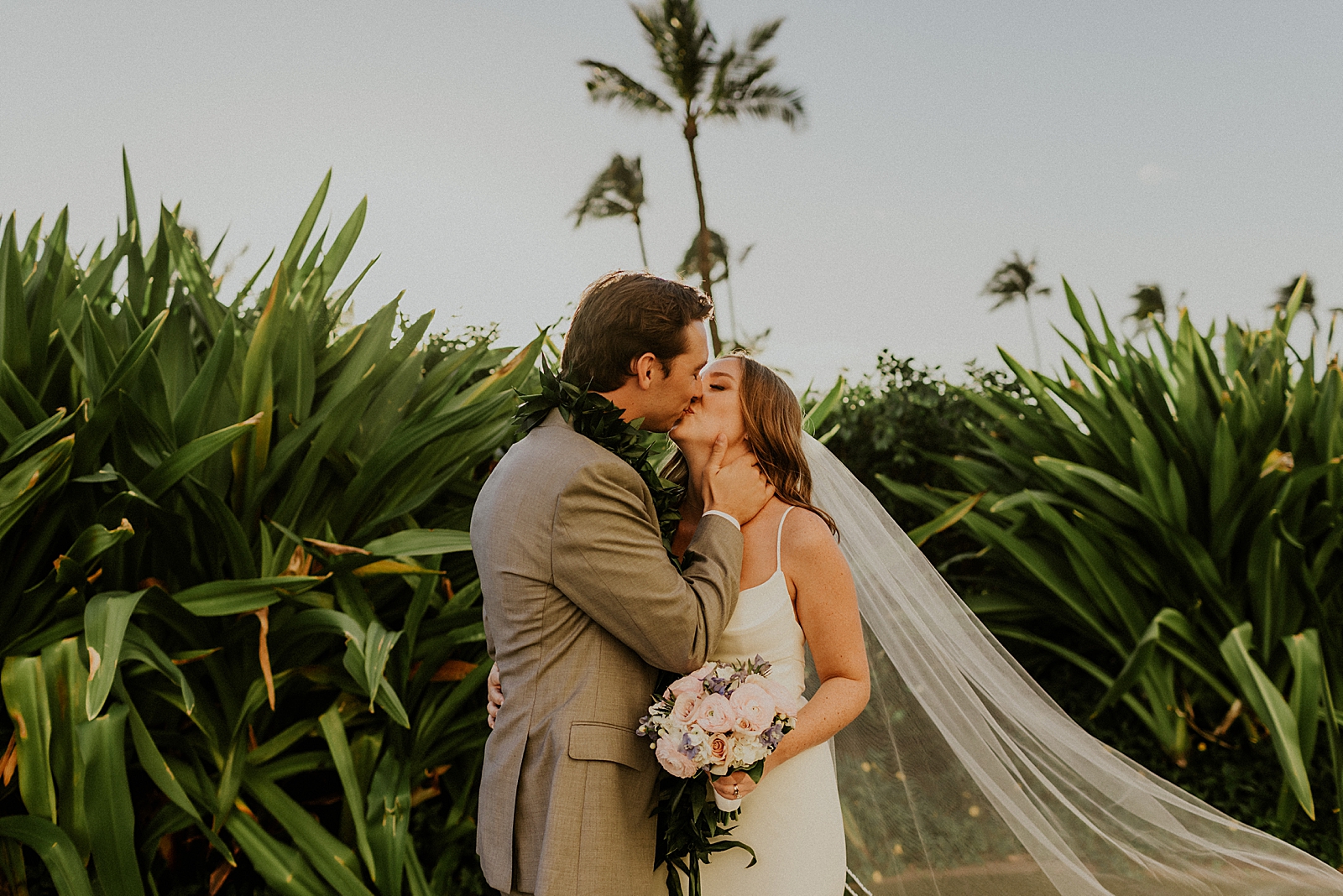 Bride and Groom kissing by tropical greenery