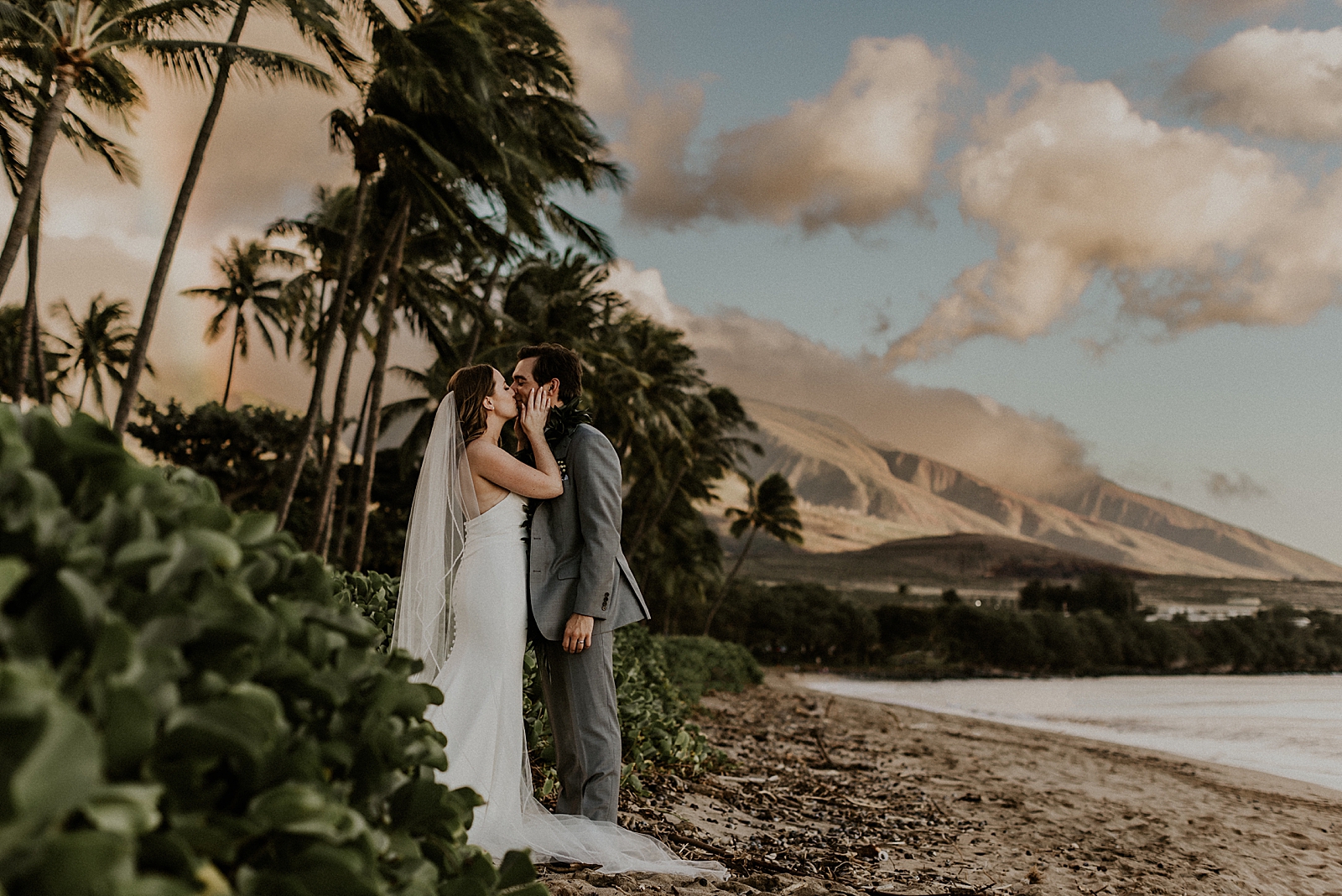 Bride holding Groom's face and kissing him with island mountain behind them