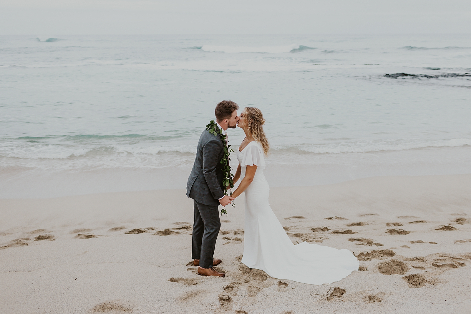 Bride and Groom holding hands and kissing on the beach by the water