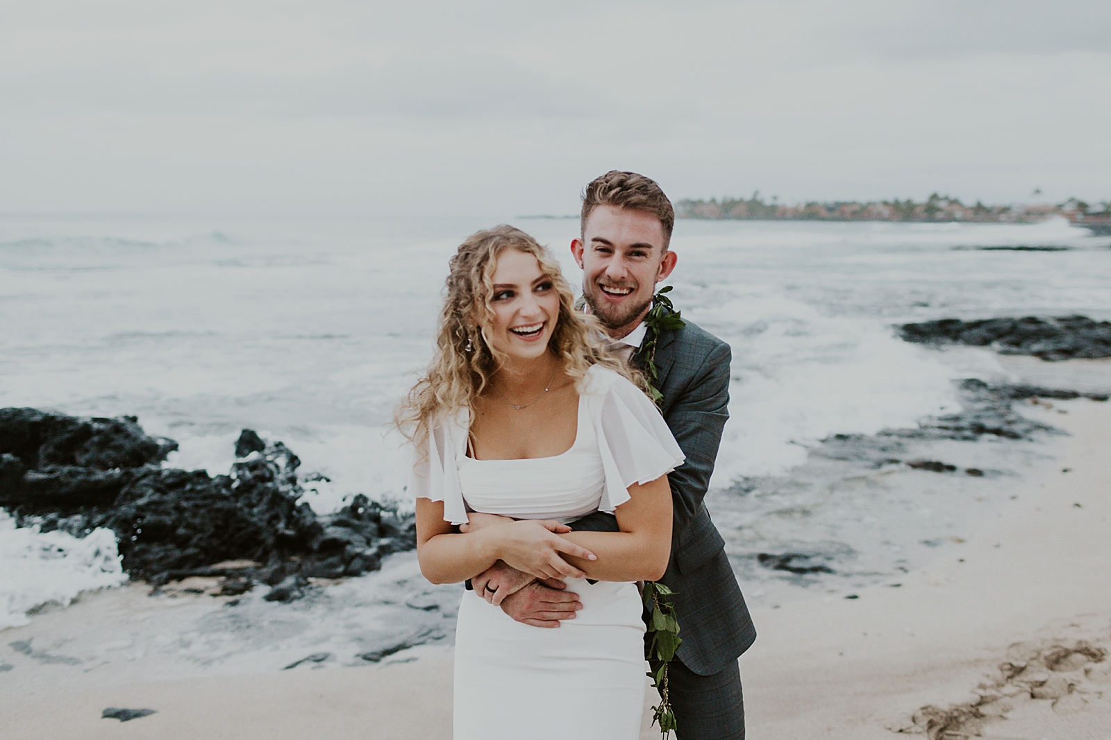 Groom holding Bride by the Oceanside with rocks