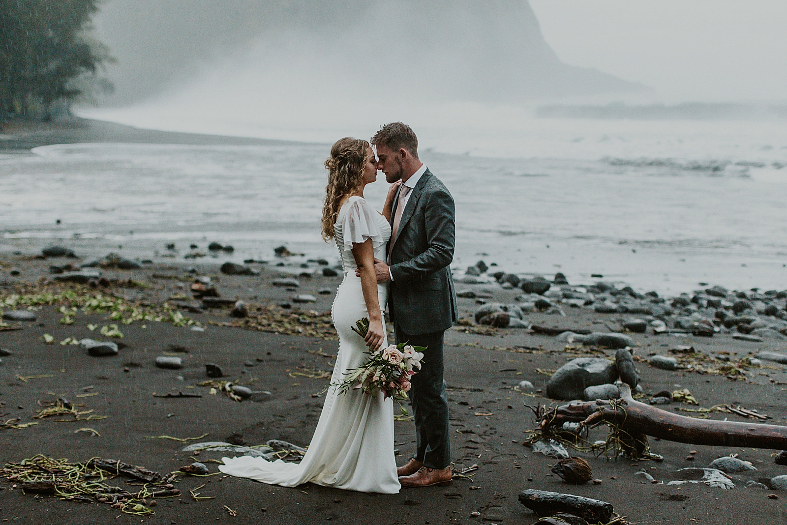Bride and Groom touching noses on the dark sand by the water