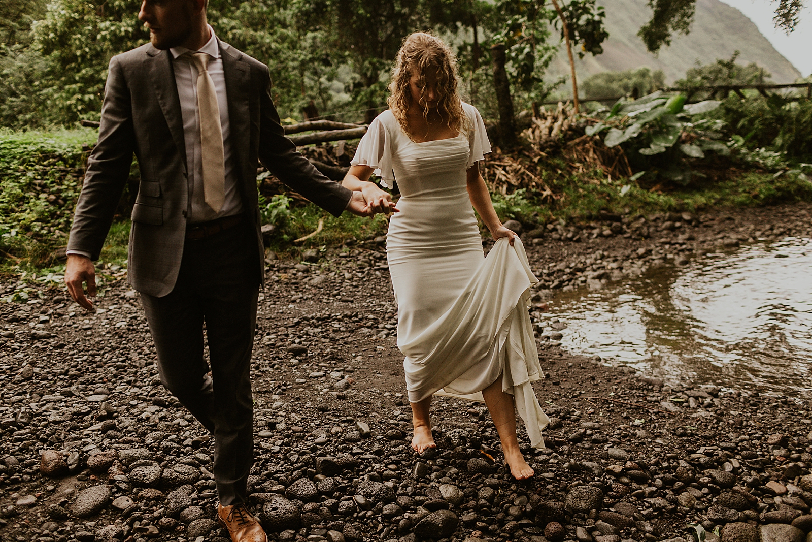 Bride and Groom walking on wet rocks by the forest