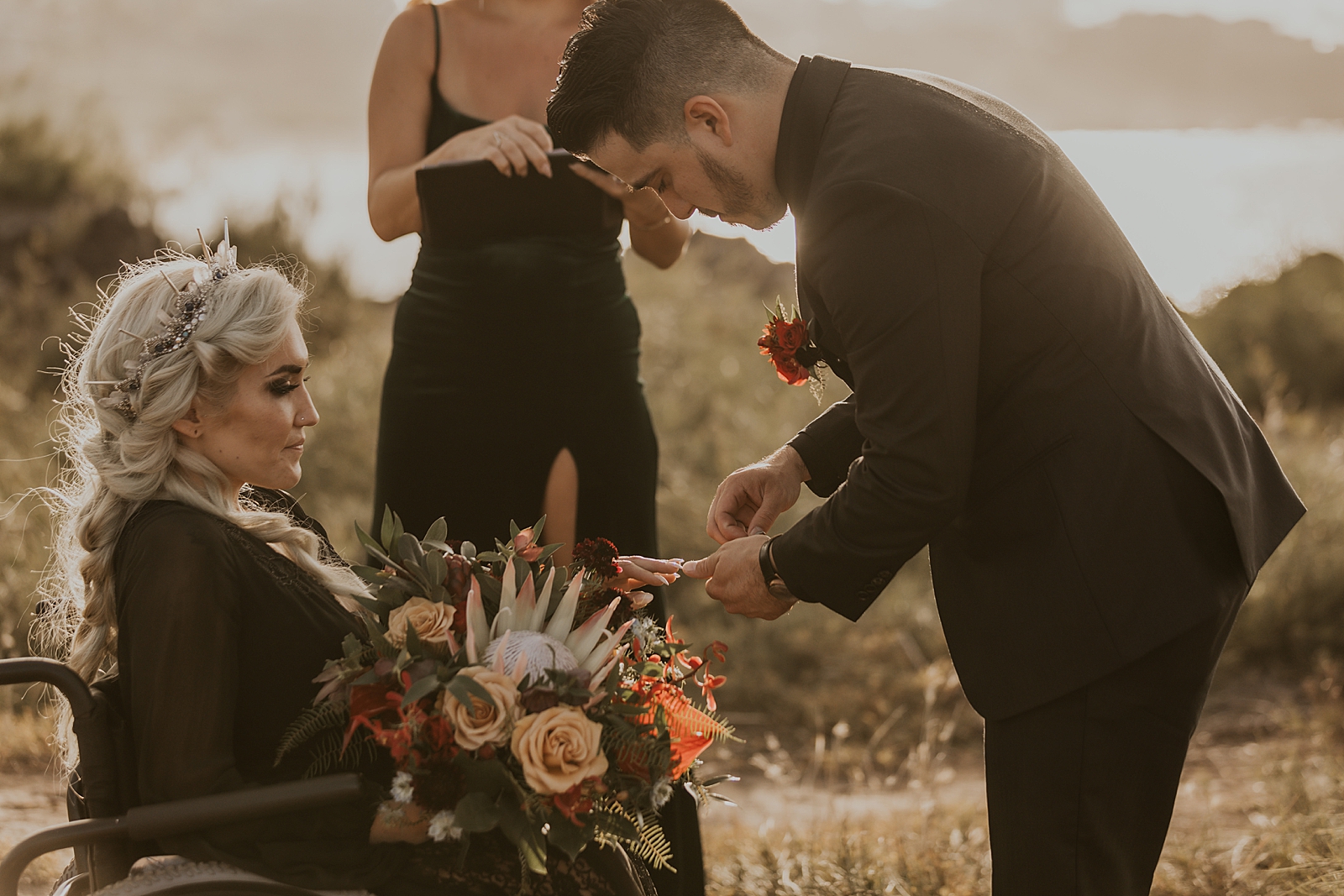 Groom leaning forward to out ring on Bride in wheel chair for outdoor Ceremony