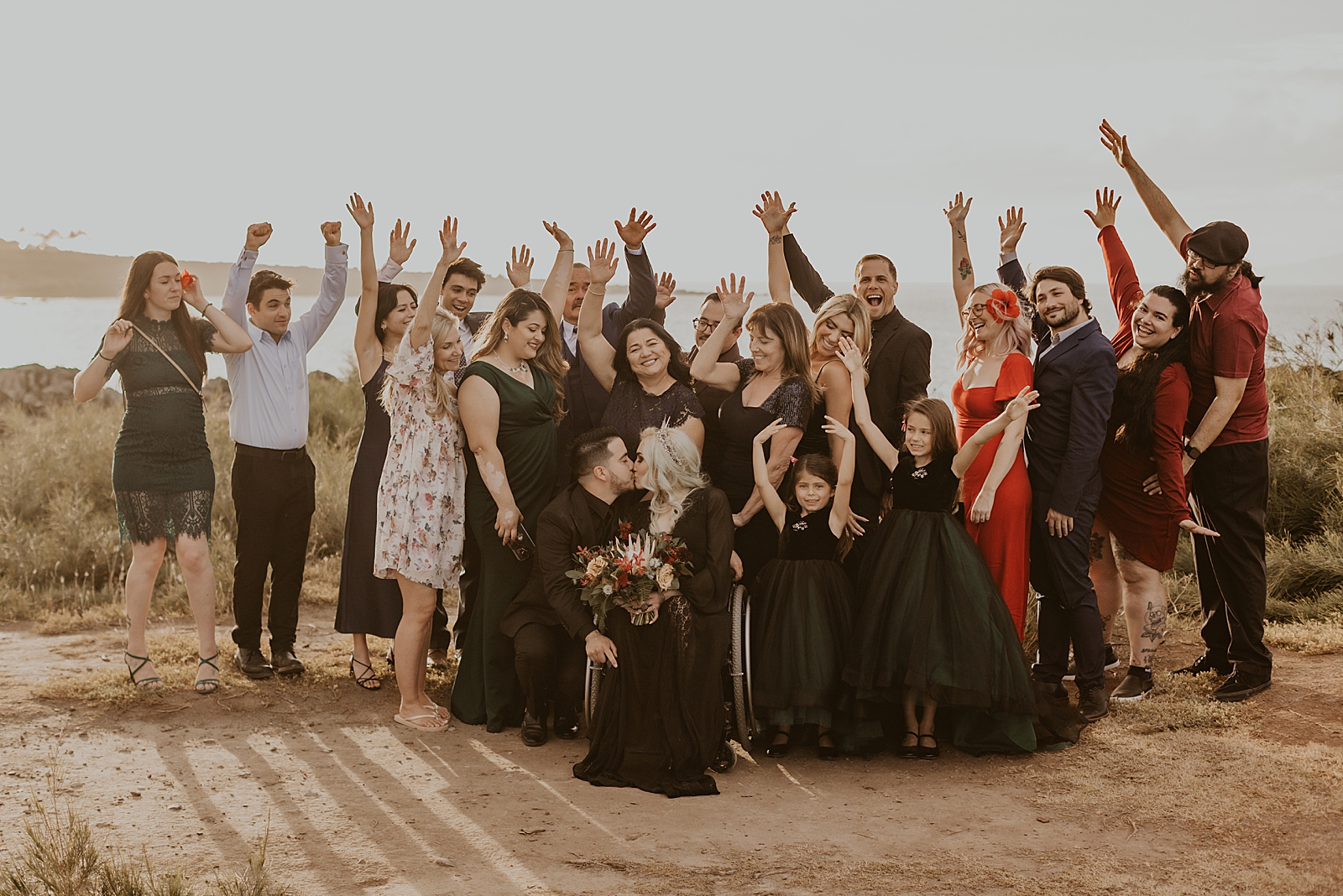 Family portrait of inter-able Bride and Groom kissing and family raising hands celebrating by the cliff side