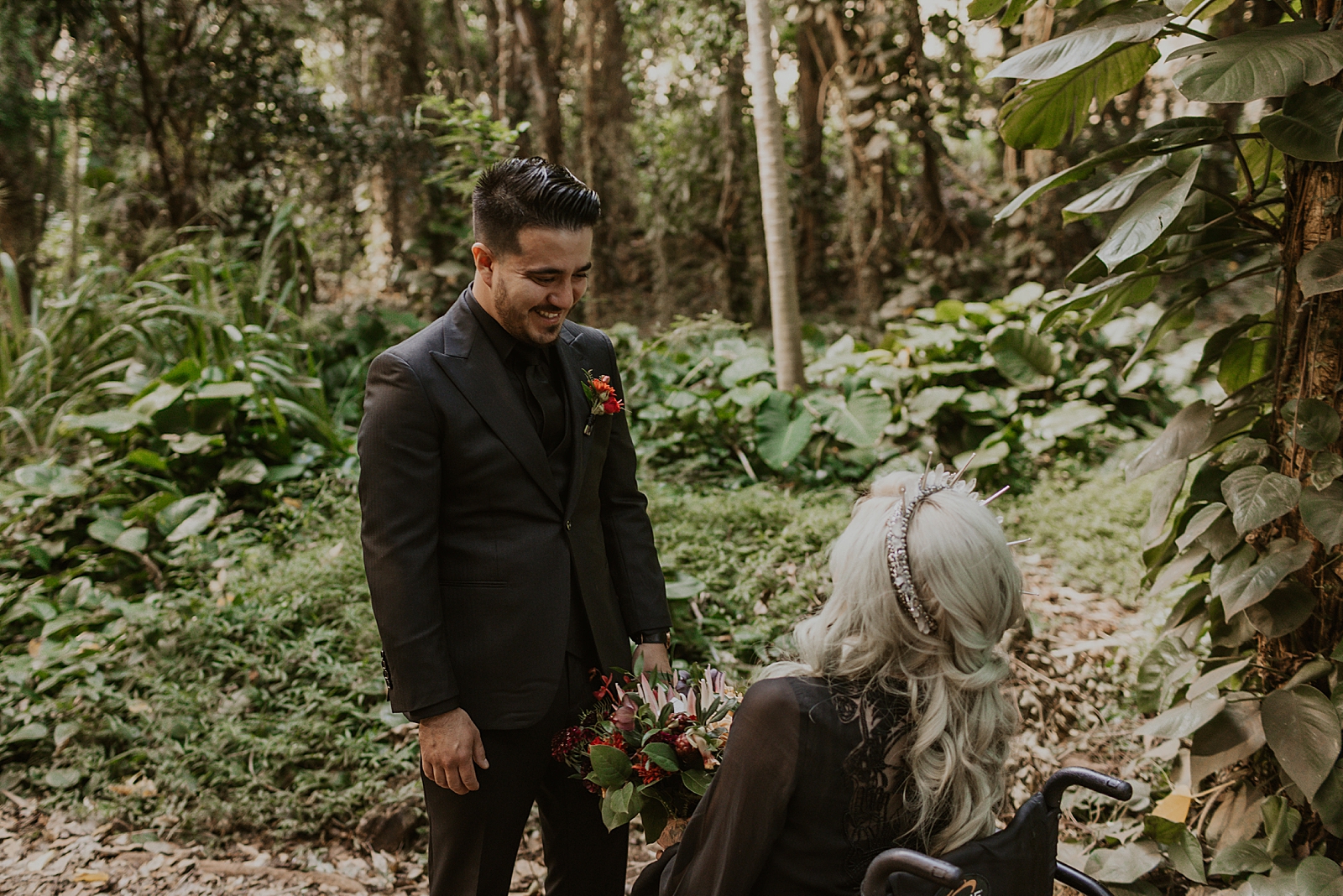 Groom's reaction to seeing Bride with bouquet in wheel chair in tropical forrest