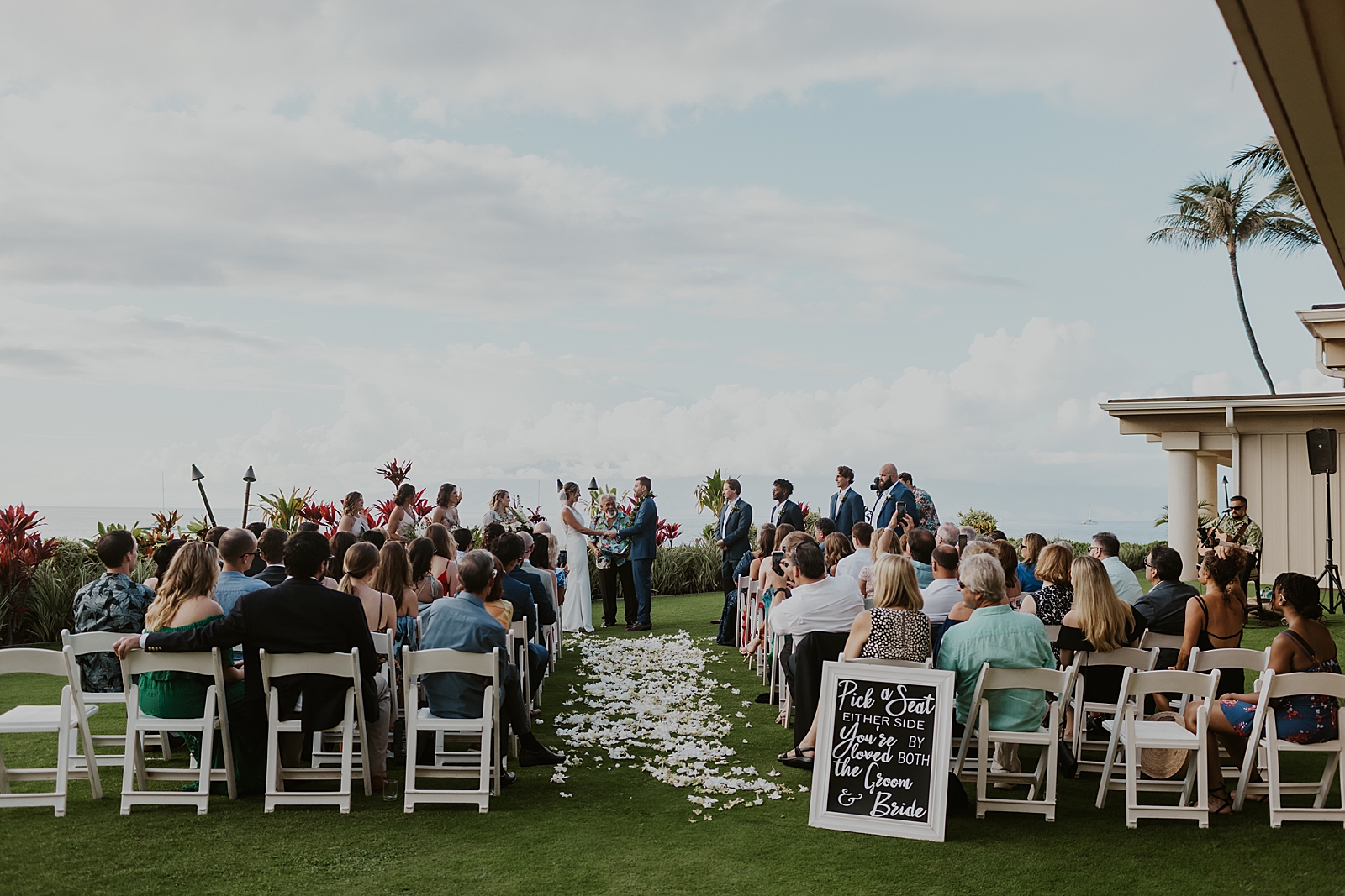 Wide shot of Bride and Groom holding hands with guests watching
