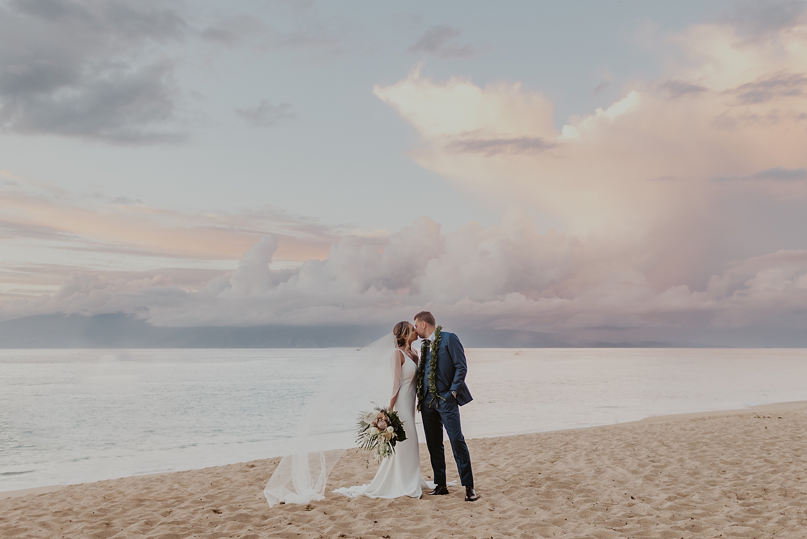 Bride and Groom kissing on the Beach with beautiful clouds by the ocean