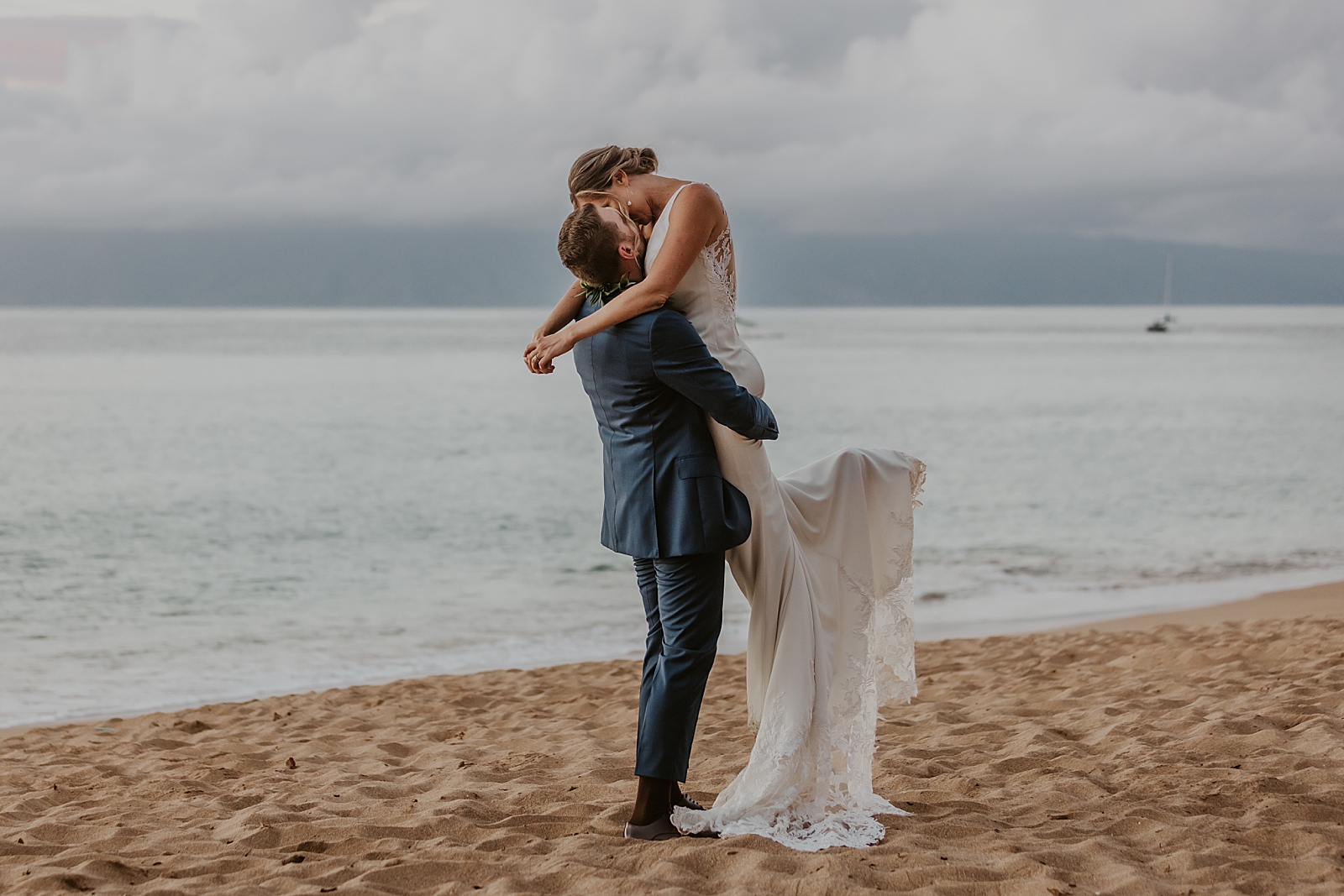 Groom holding up Bride and kissing by the ocean