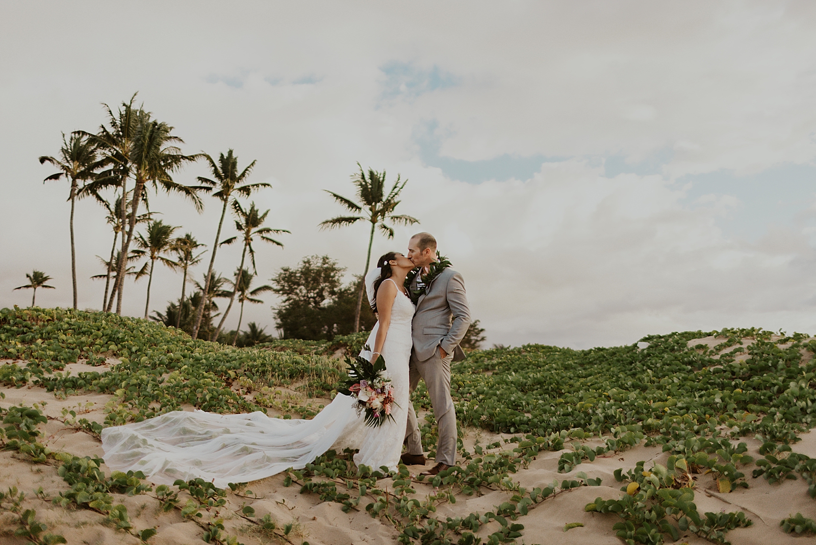 Bride and Groom kissing on sandy and green hillside of the beach