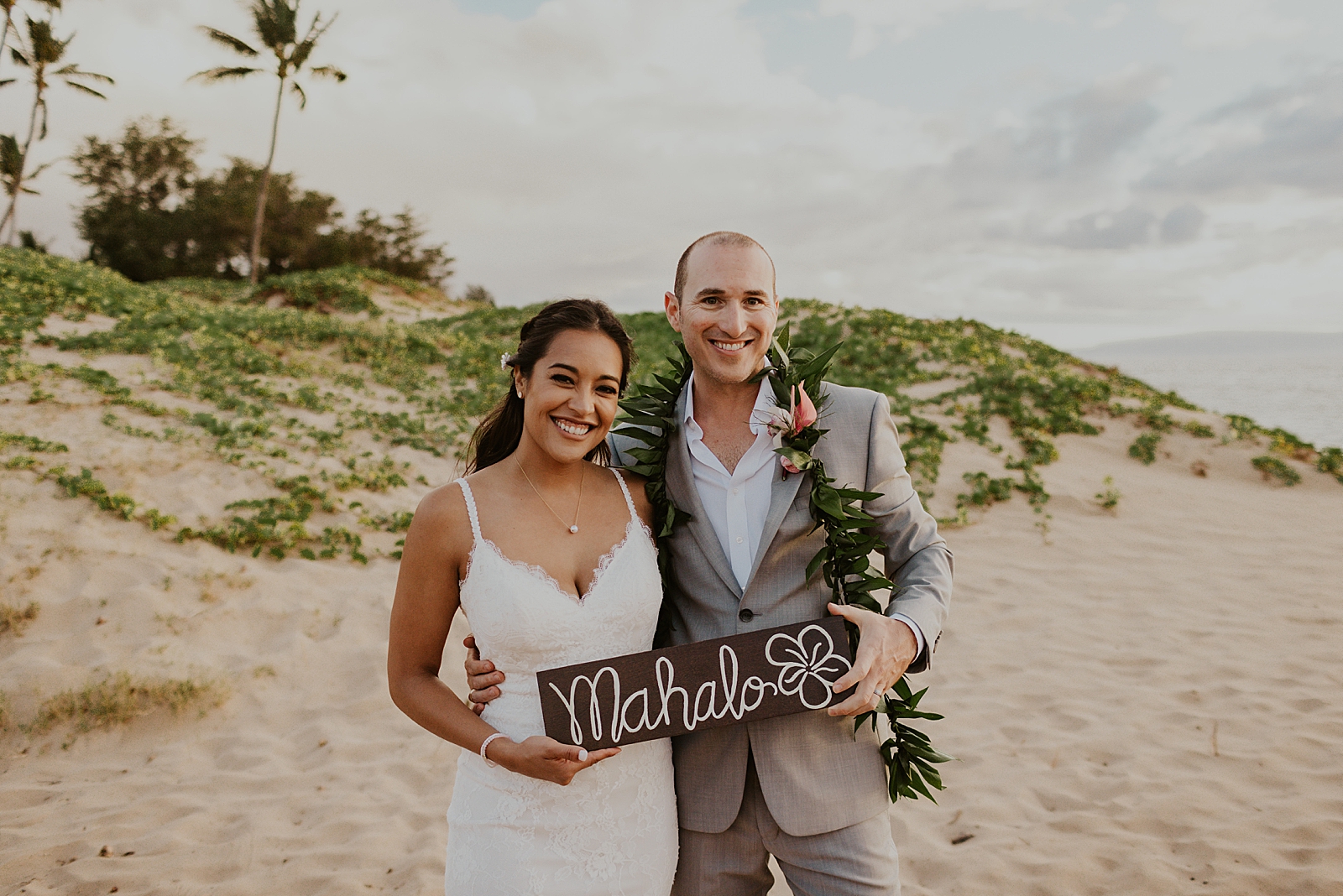 Bride and Groom portrait of them holding "Mahalo" sign on the beach