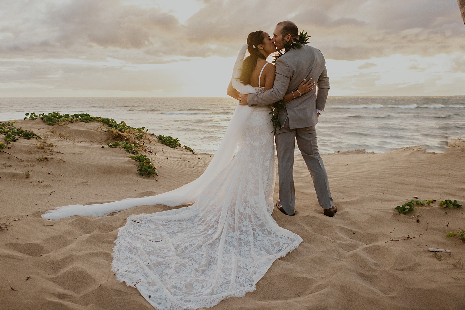 Bride and Groom kissing standing on the sand of the the beach with the ocean in front of them