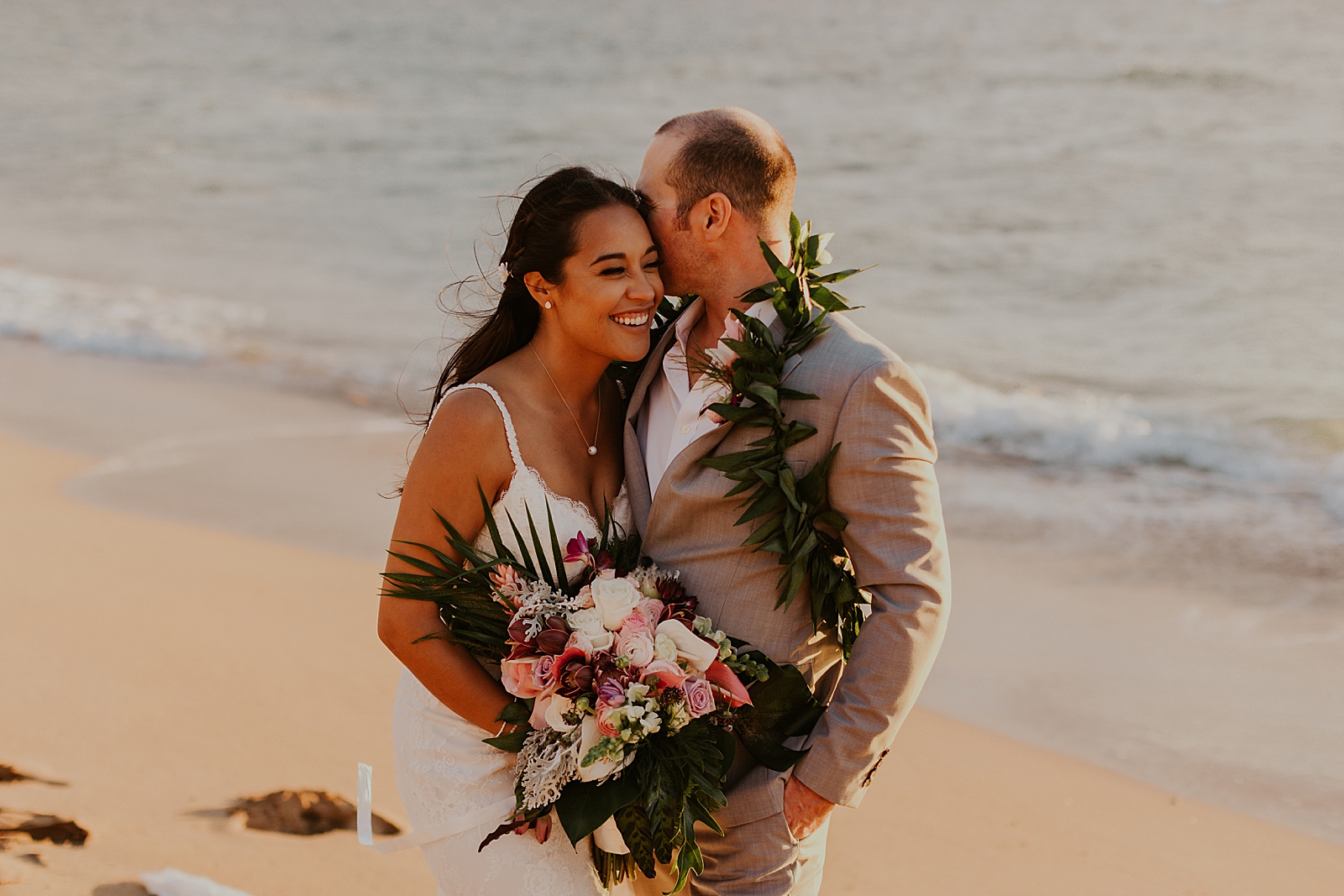 Groom holding and nuzzling bride on next to the ocean