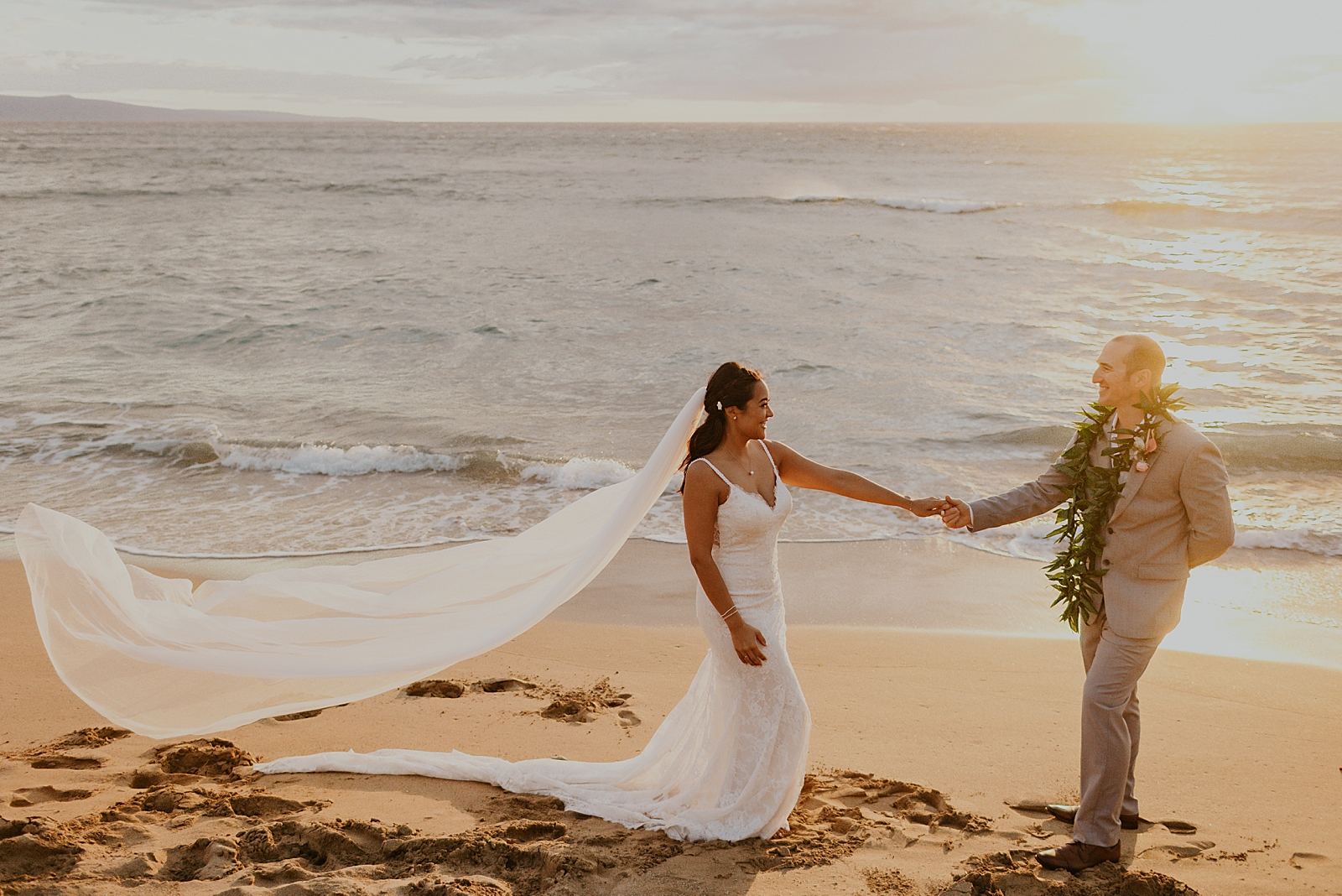 Bride and Groom extending and holding each others hands and veil flowing with the sun setting 