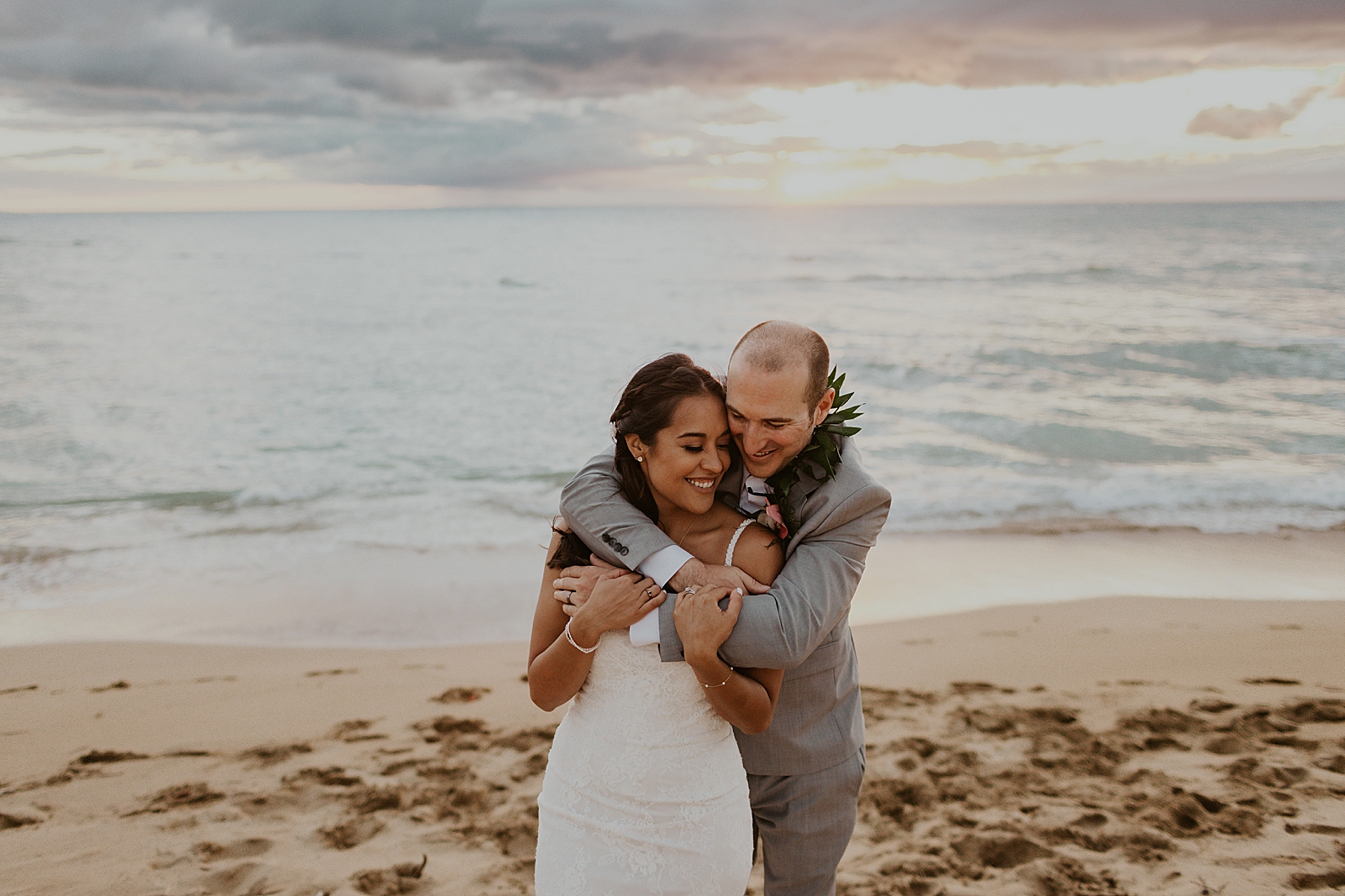 groom holding Bride from behind on the beach