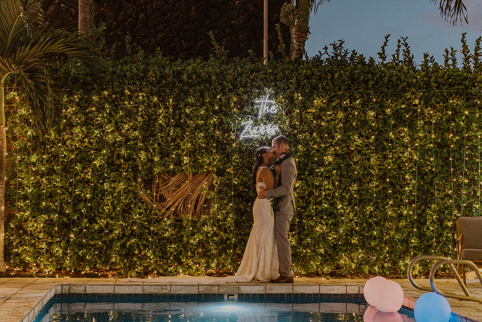 Bride and Groom kissing by the pool in front of light up sign of their last name