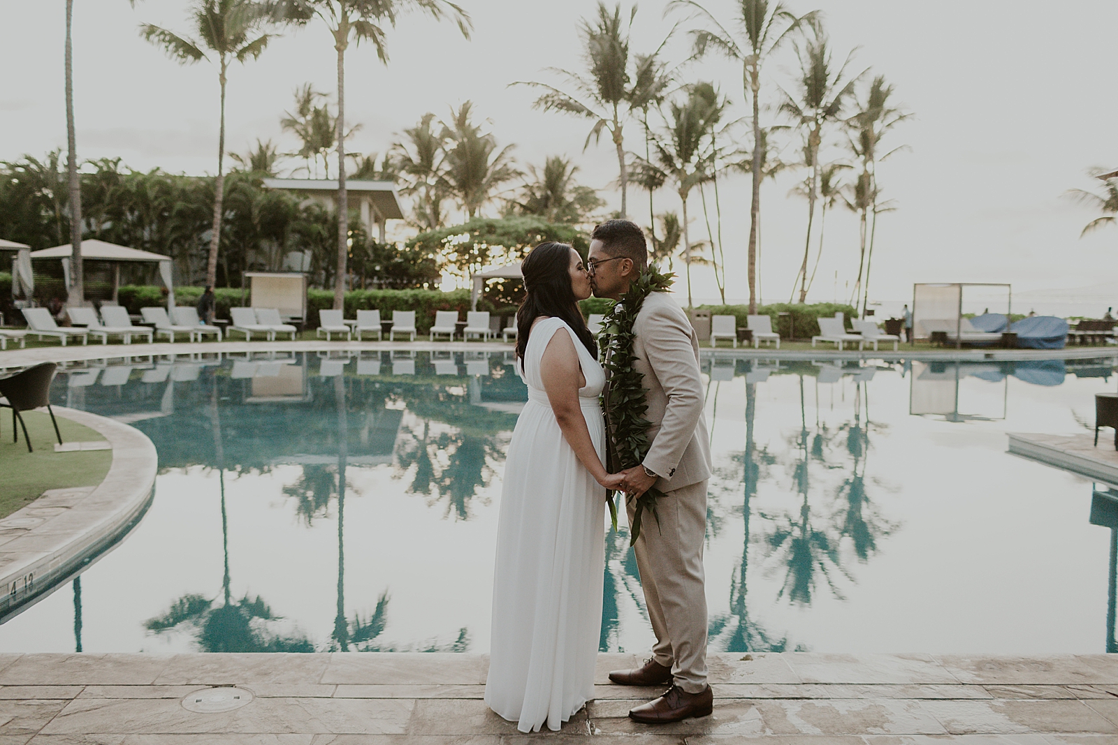 Bride and Groom holding hands and kissing in front of a pool