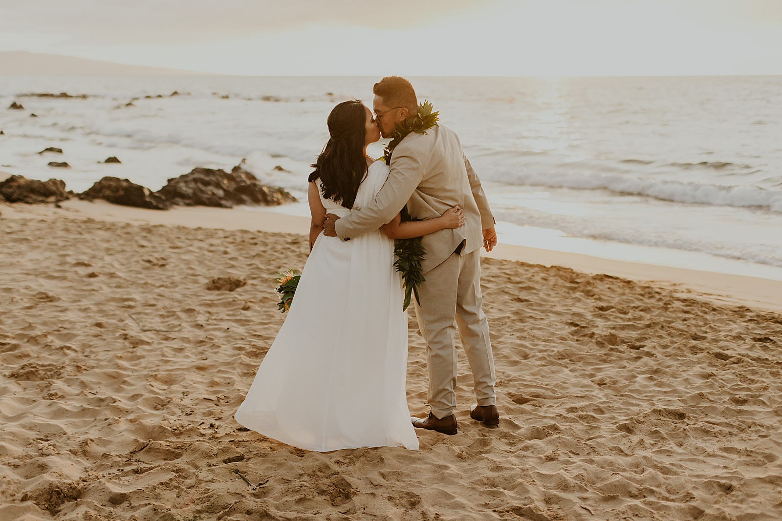 Bride and Groom kissing while on the beach with the sun setting