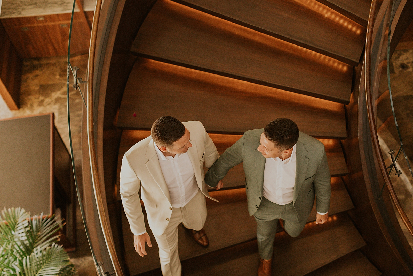 Grooms holding hands walking down spiral staircase