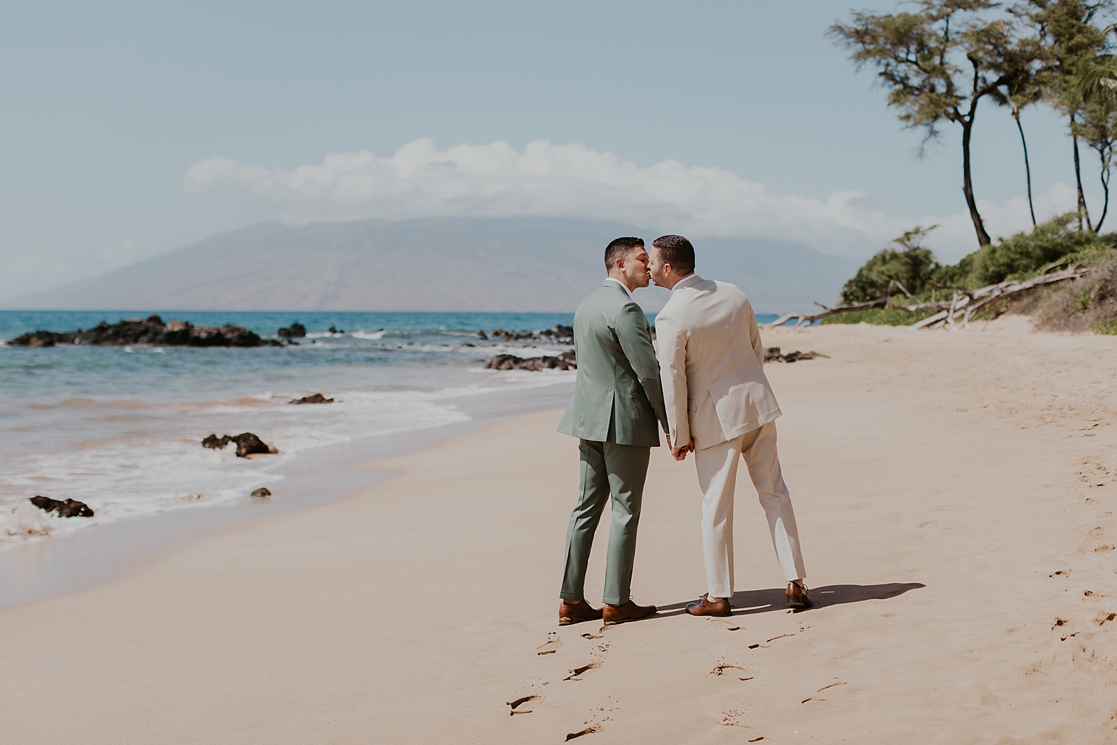 Grooms kissing while walking on the beach by the water