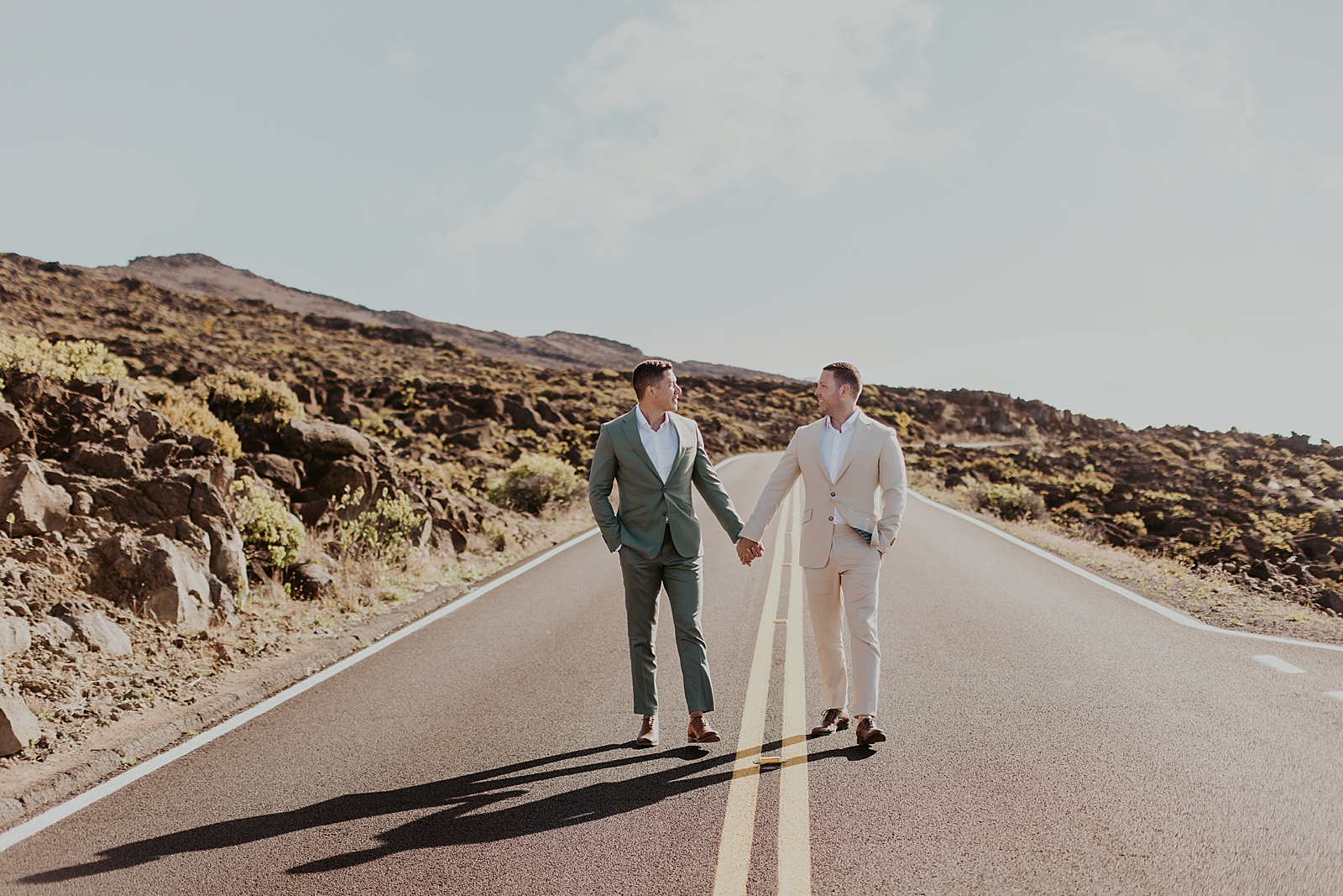 Grooms holding hands while standing on the open road