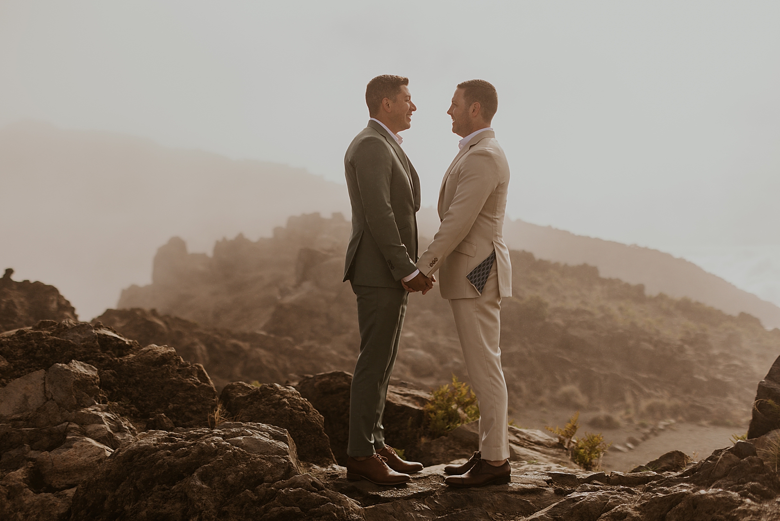 Grooms holding hands and looking at each other while standing on rocks