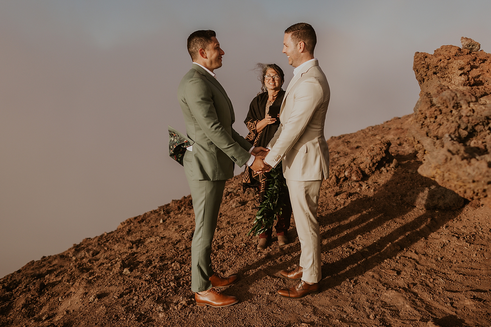 Grooms holding hands with officiant out on the mountain side