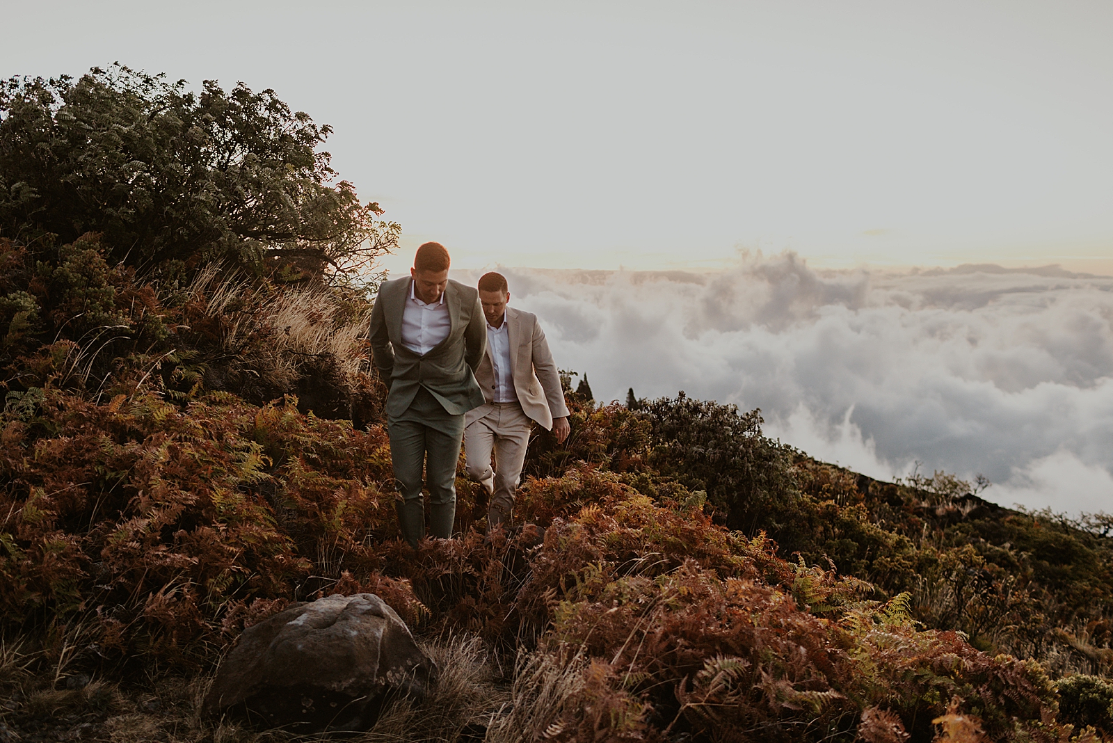 Grooms walking on mountain side and with cloud tops visible 