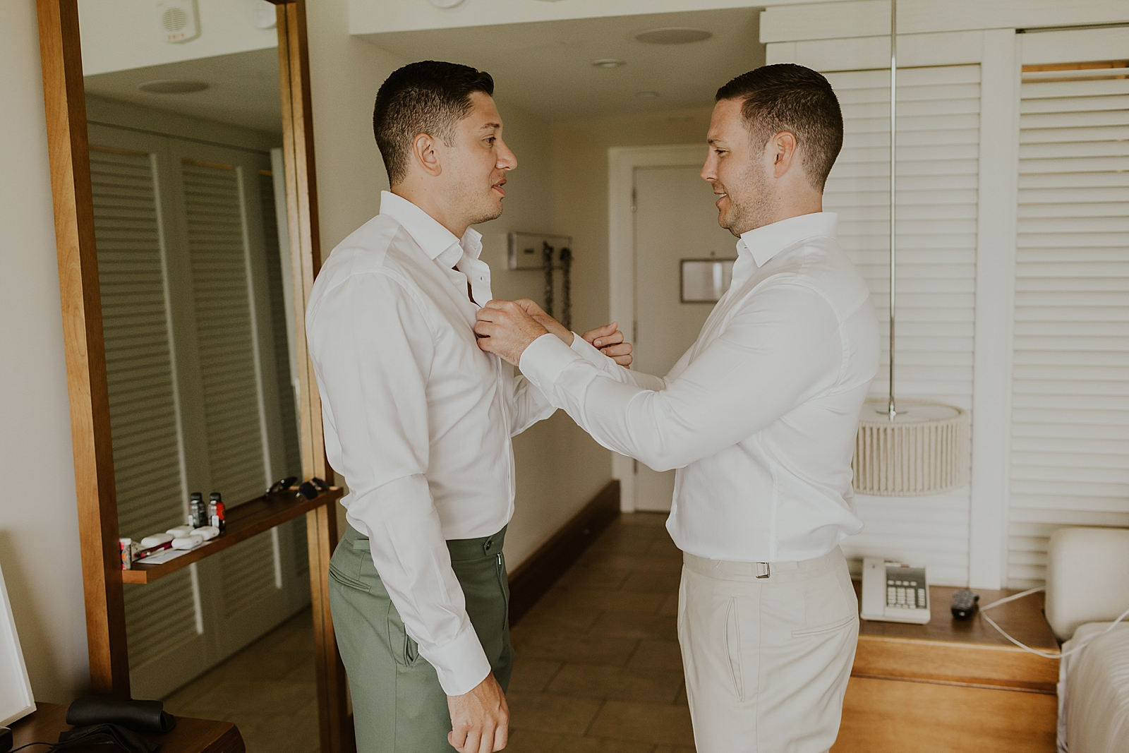 Groom getting help buttoning shirt in hotel room