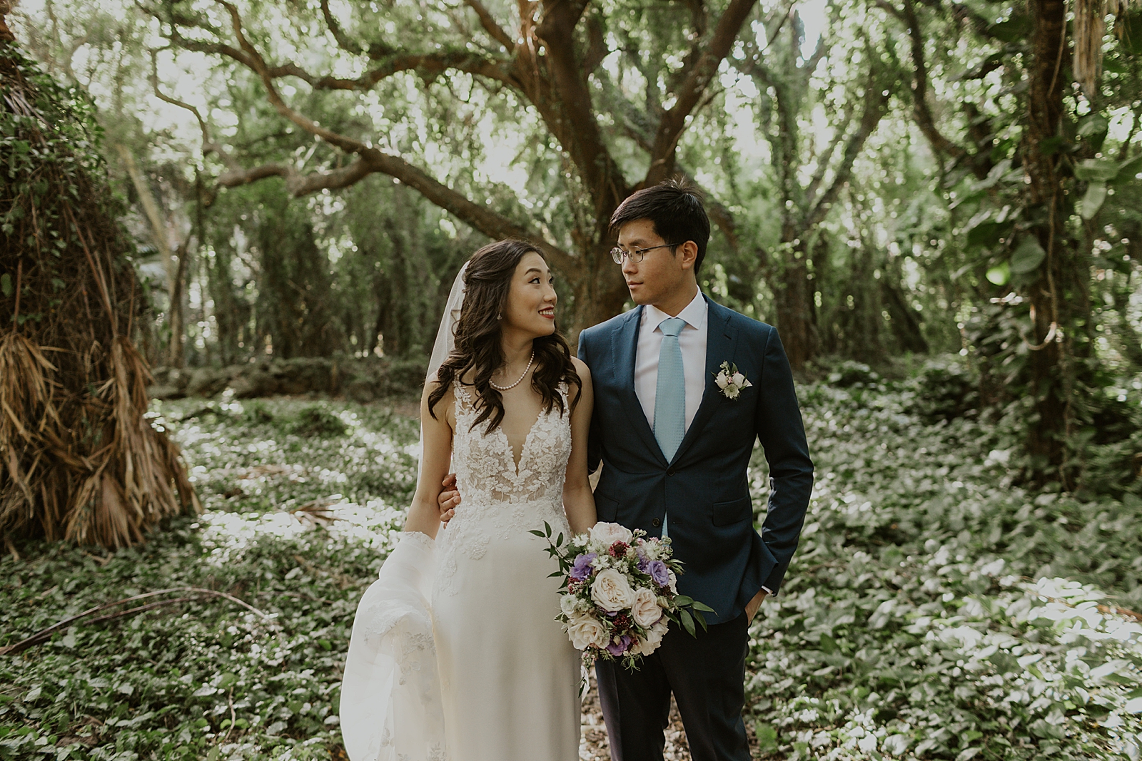 Bride and Groom side by side looking at each other surrounded by trees and greenery