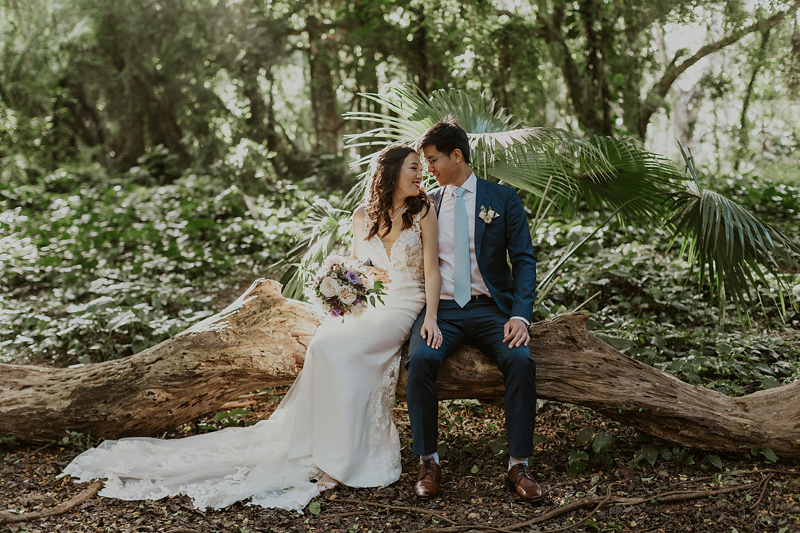 Bride and Groom sitting on fallen tree log in the forest