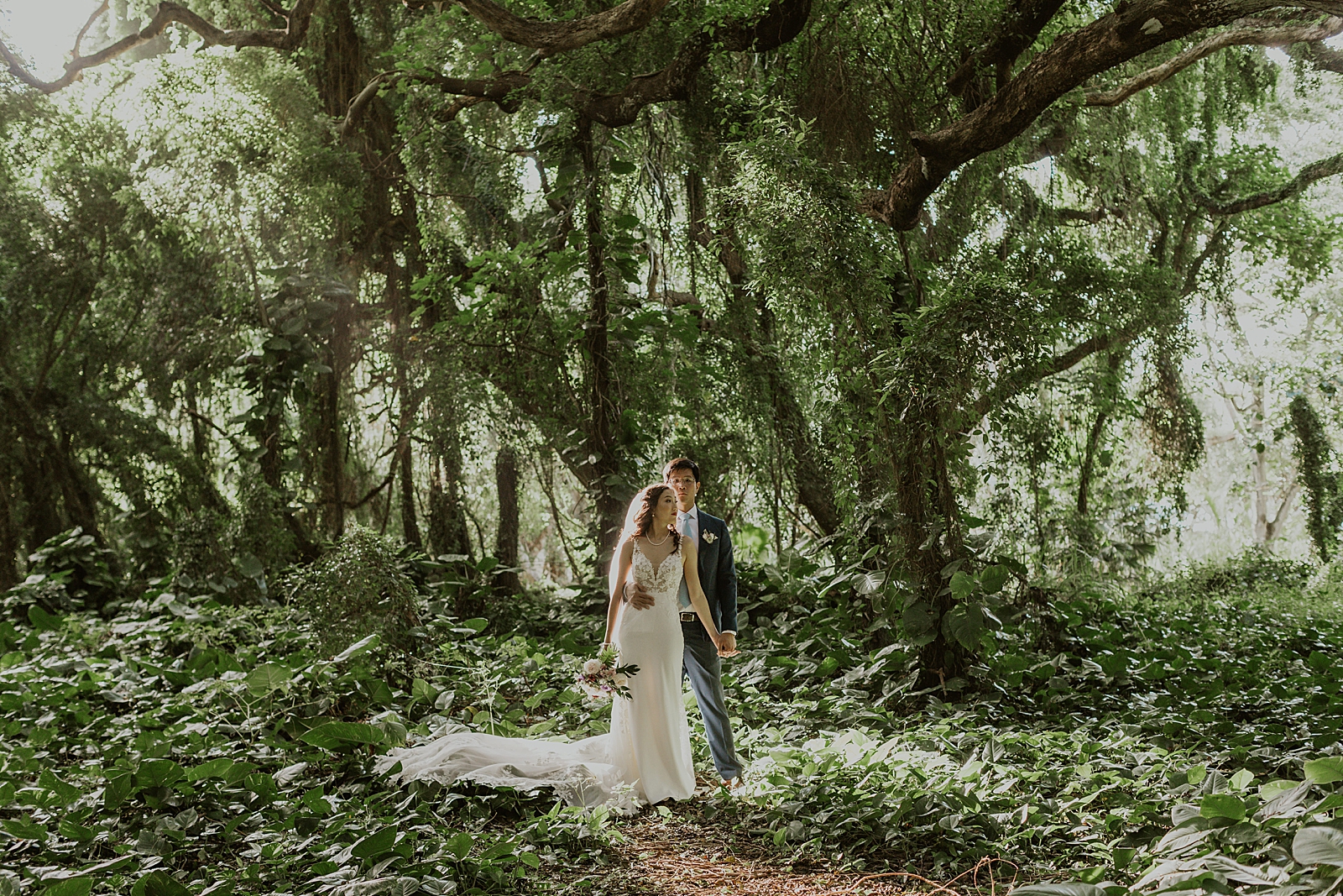 Groom holding Bride from behind in the green forest