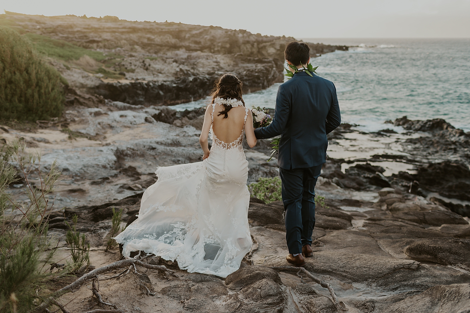 Bride and Groom walking down rocky terrain towards the ocean