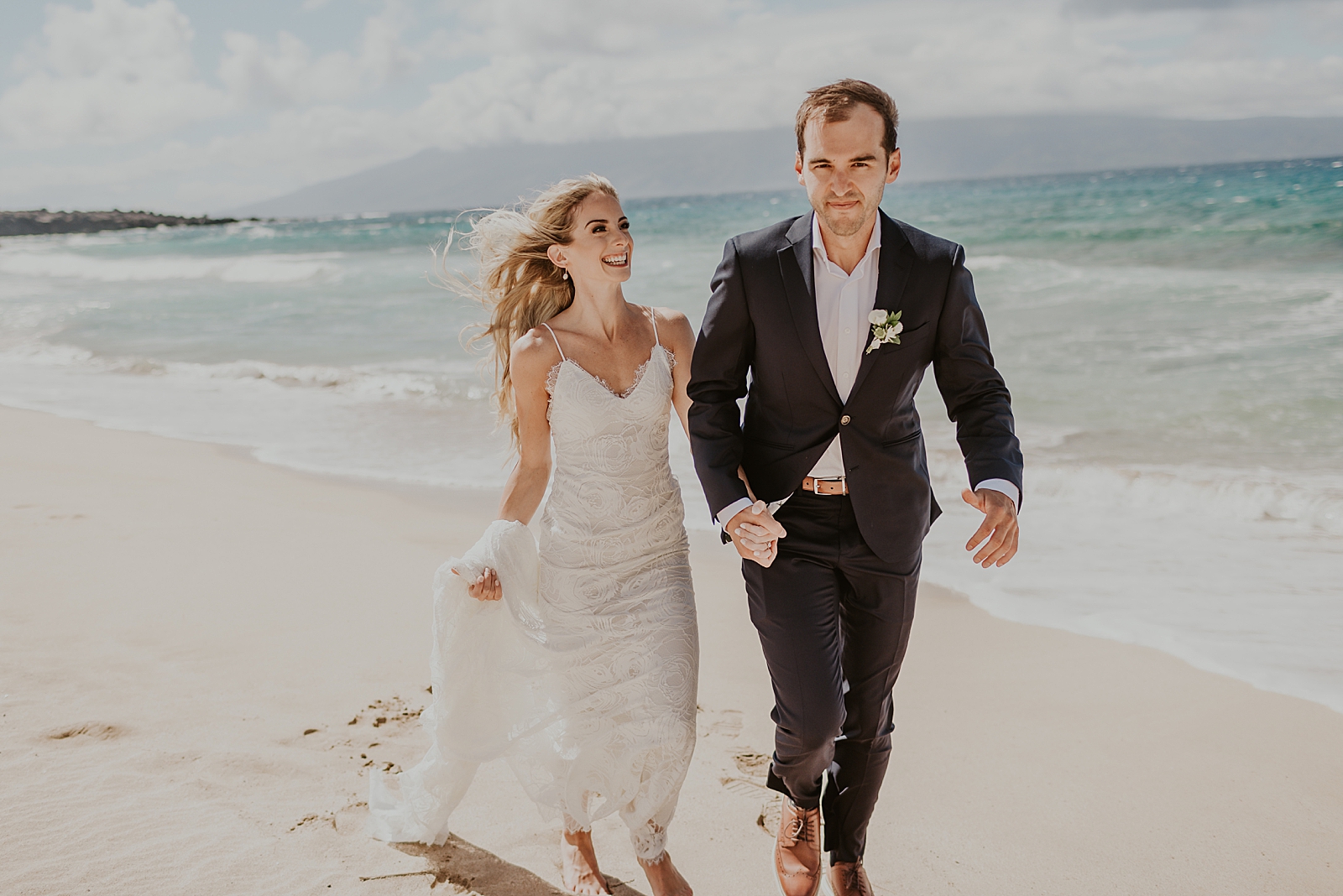 Bride and Groom holding hands and running on the beach along the ocean shoreline