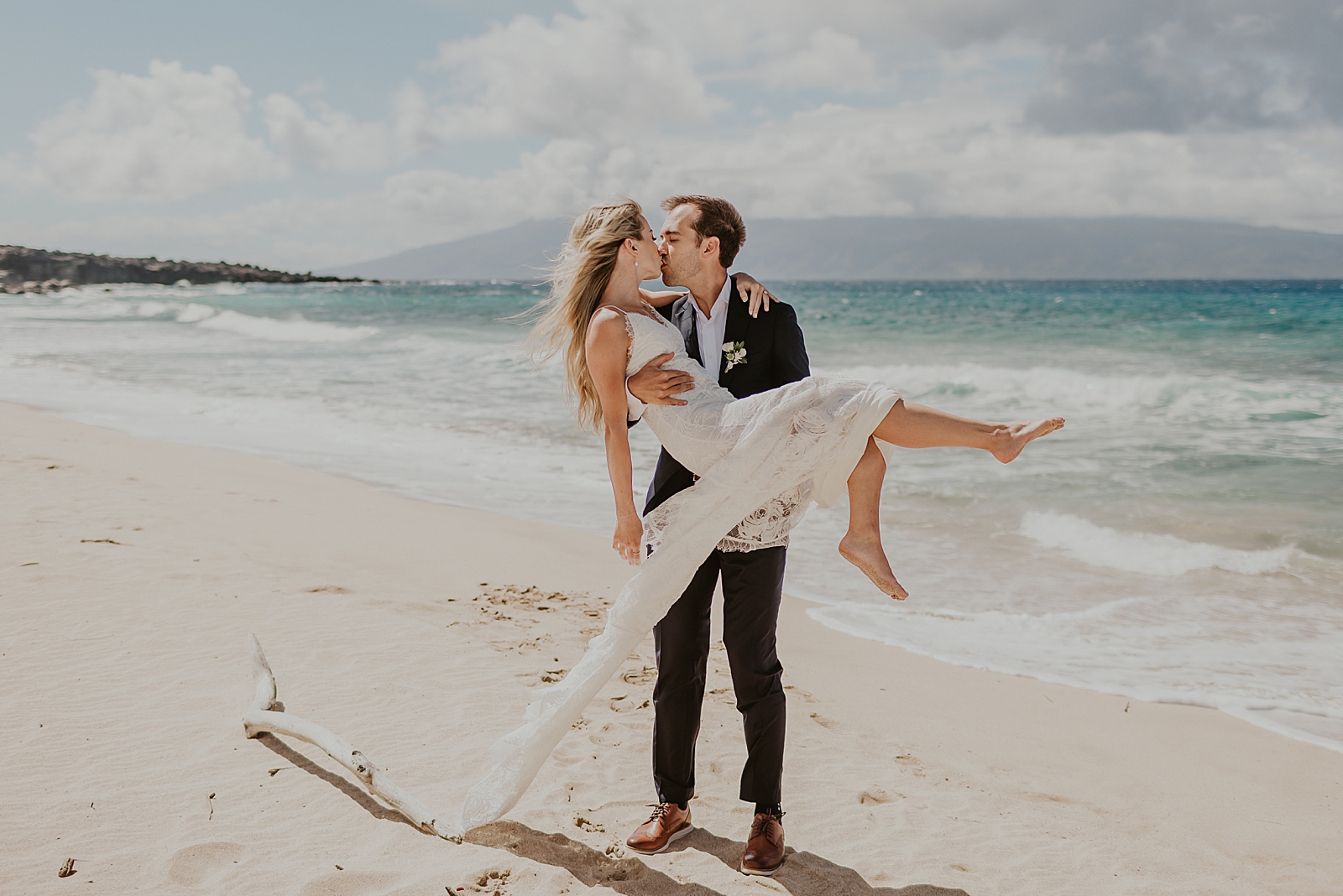 Groom holding Bride in arms and kissing her on the beach