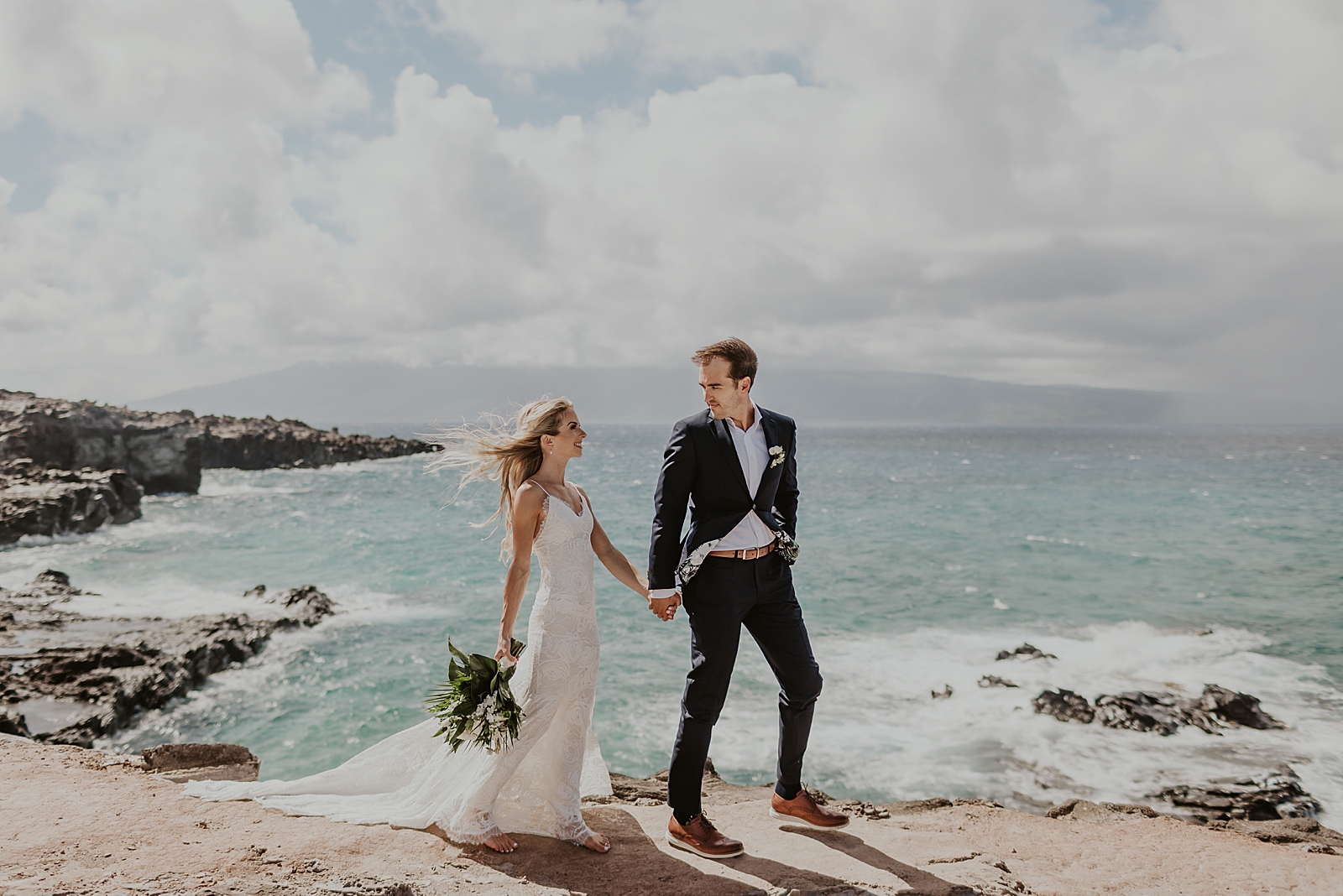 Bride and Groom holding hands as they walk by the ocean shoreline