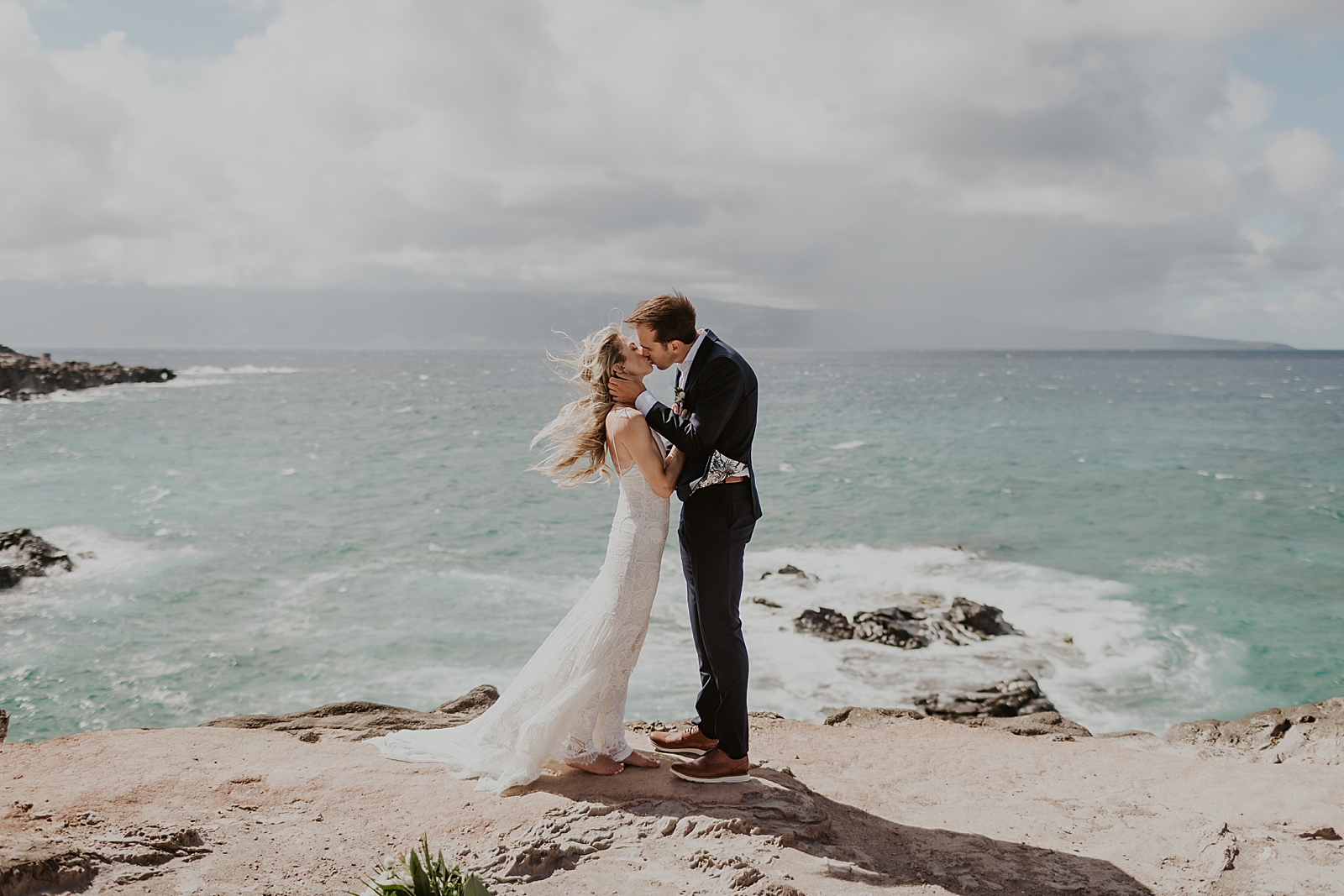 Bride and Groom holding each other and kissing in front of clear ocean water