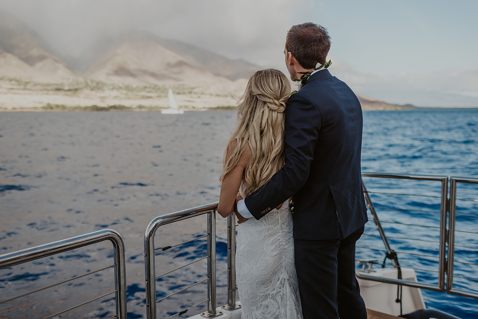 Groom holding Bride and both of them looking out at the land while out on a boat