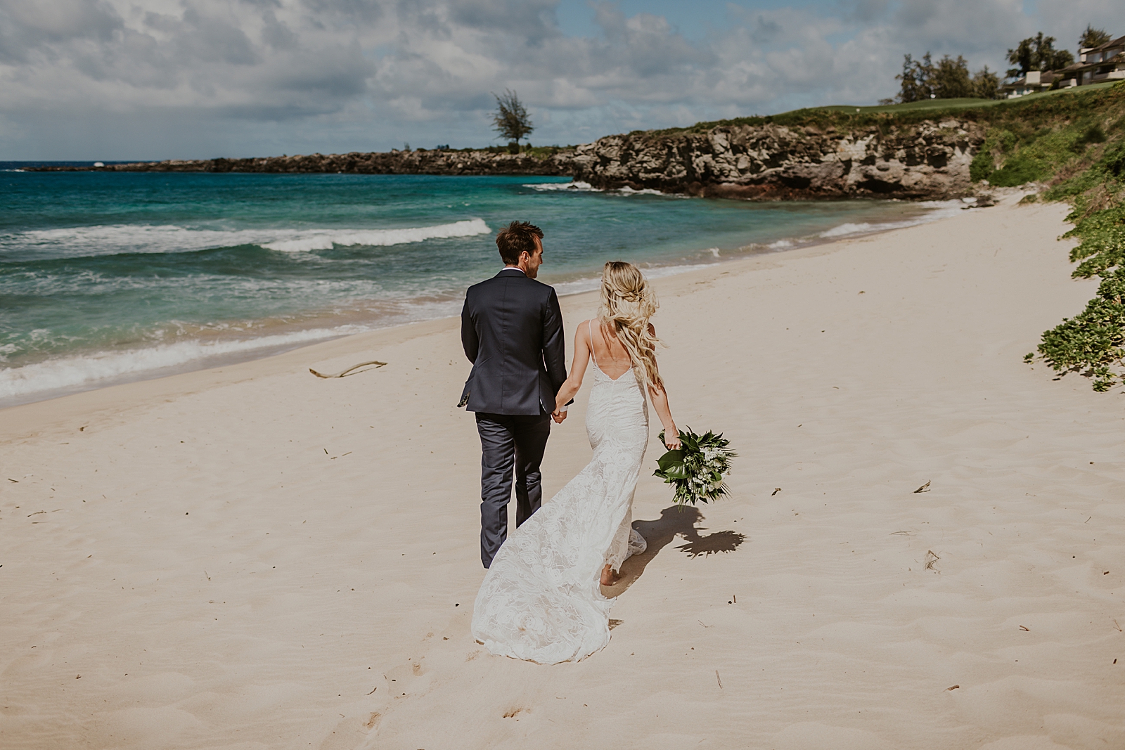 Bride and Groom holding hands walking on the beach with the ocean in sight
